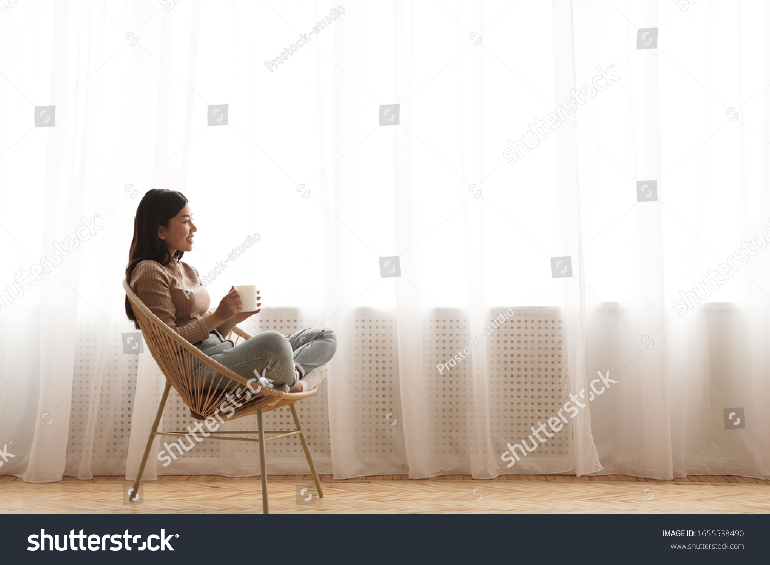 Tea time. Relaxed girl sitting in modern chair, enjoying hot coffee in front of window, side view, free space #1655538490