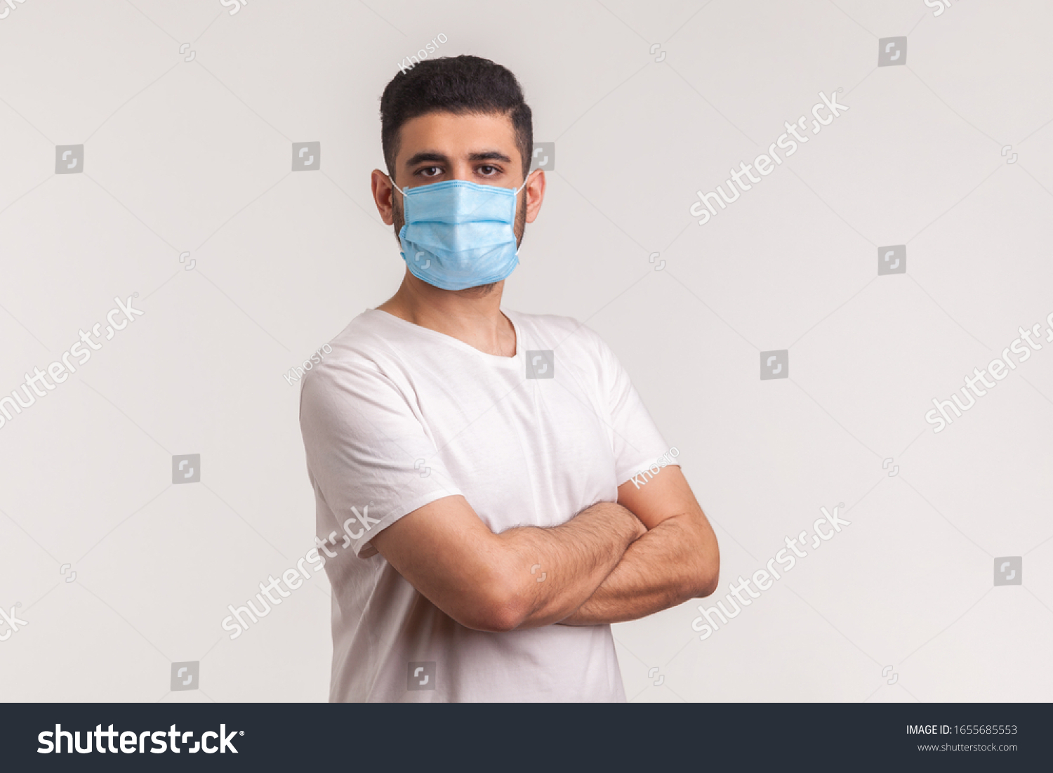 Effective protection against coronavirus. Man holding hands crossed and wearing hygienic mask to prevent infection, respiratory illness such as flu, 2019-nCoV, Covid-19. indoor studio shot, white back #1655685553