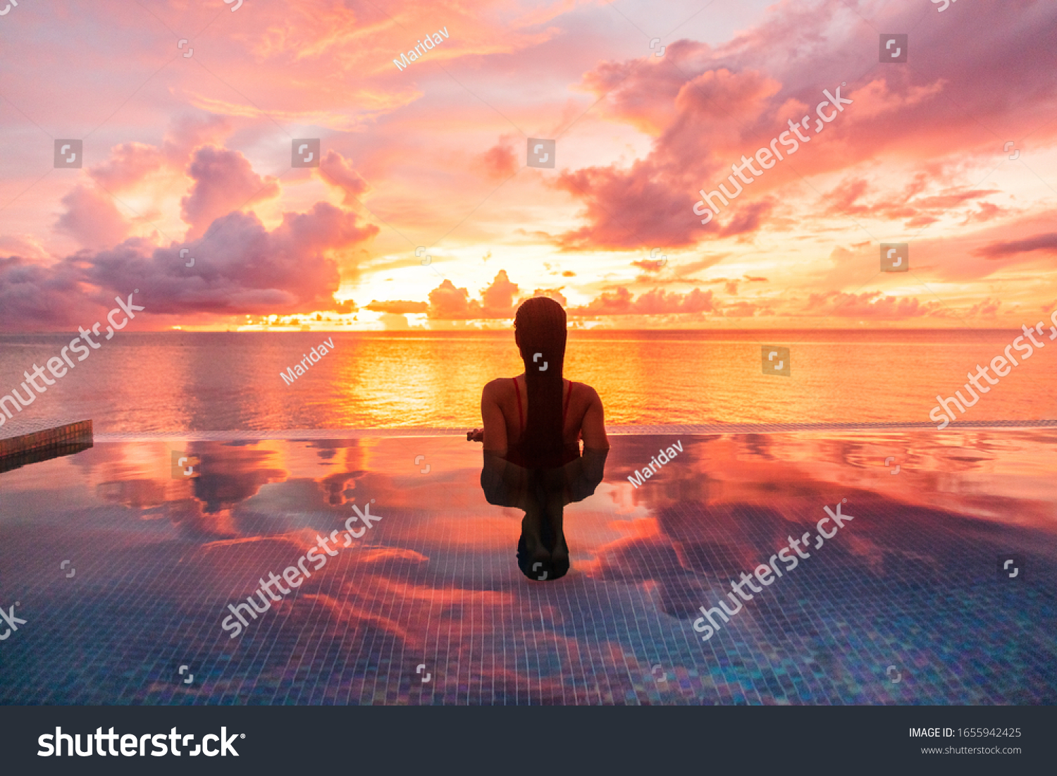 Paradise luxury resort honeymoon getaway destination at idyllic Caribbean tropical landscape hotel, woman silhouette swimming in infinity pool watching sunset serene. Winter getaway at dusk. #1655942425