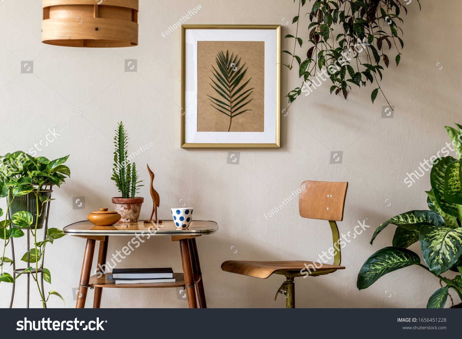 Retro interior design of living room with stylish vintage chair and table, plants, cacti, personal accessories and gold mock up poster frame on the beige wall. Elegant home decor. Template.  #1656451228