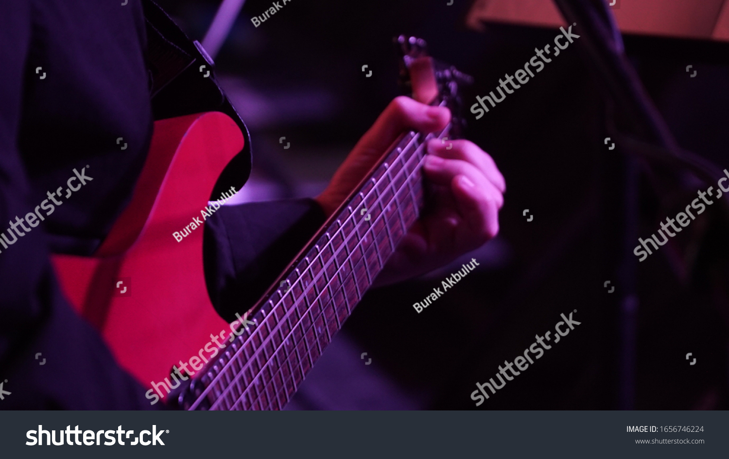 Man playing music with an electro guitar in the concert. Photography of the musician plays the electro guitar. He picks the strings, clamps the strings on the fretboard. High resolution image. #1656746224