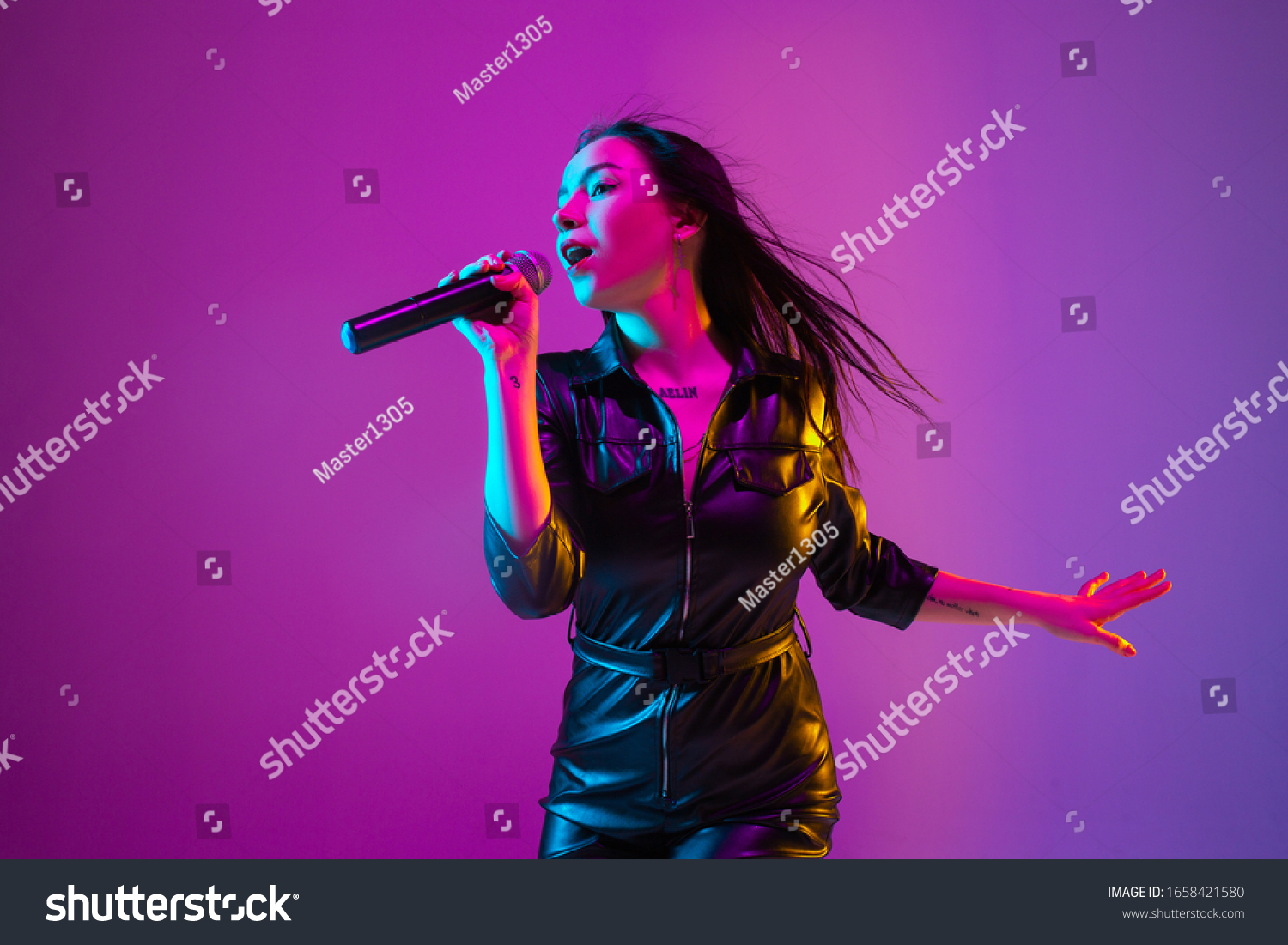 Caucasian female singer portrait isolated on purple studio background in neon light. Beautiful female model in black wear with microphone. Concept of human emotions, facial expression, ad, music, art. #1658421580