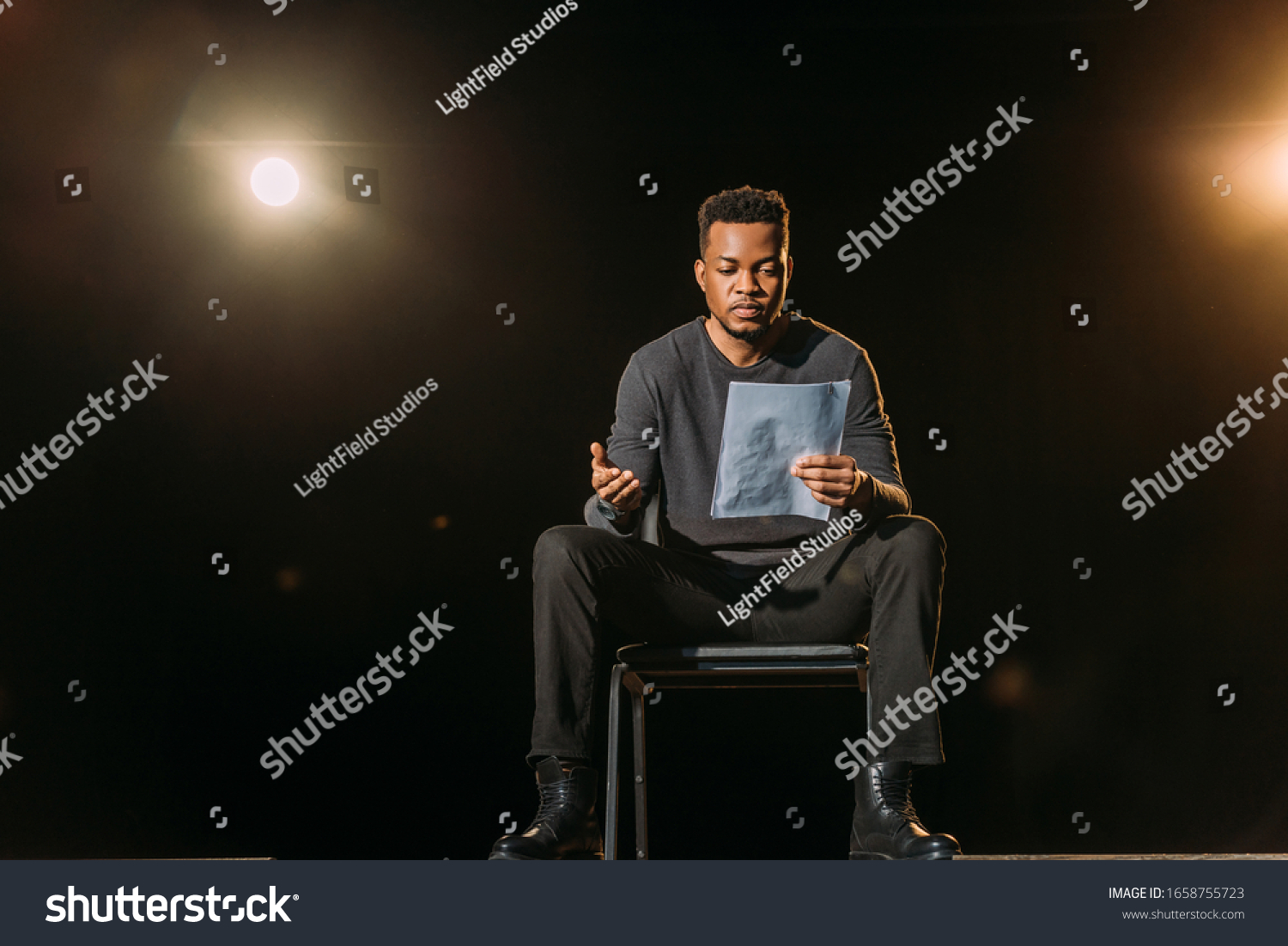 handsome african american actor holding scenario on stage during rehearse #1658755723