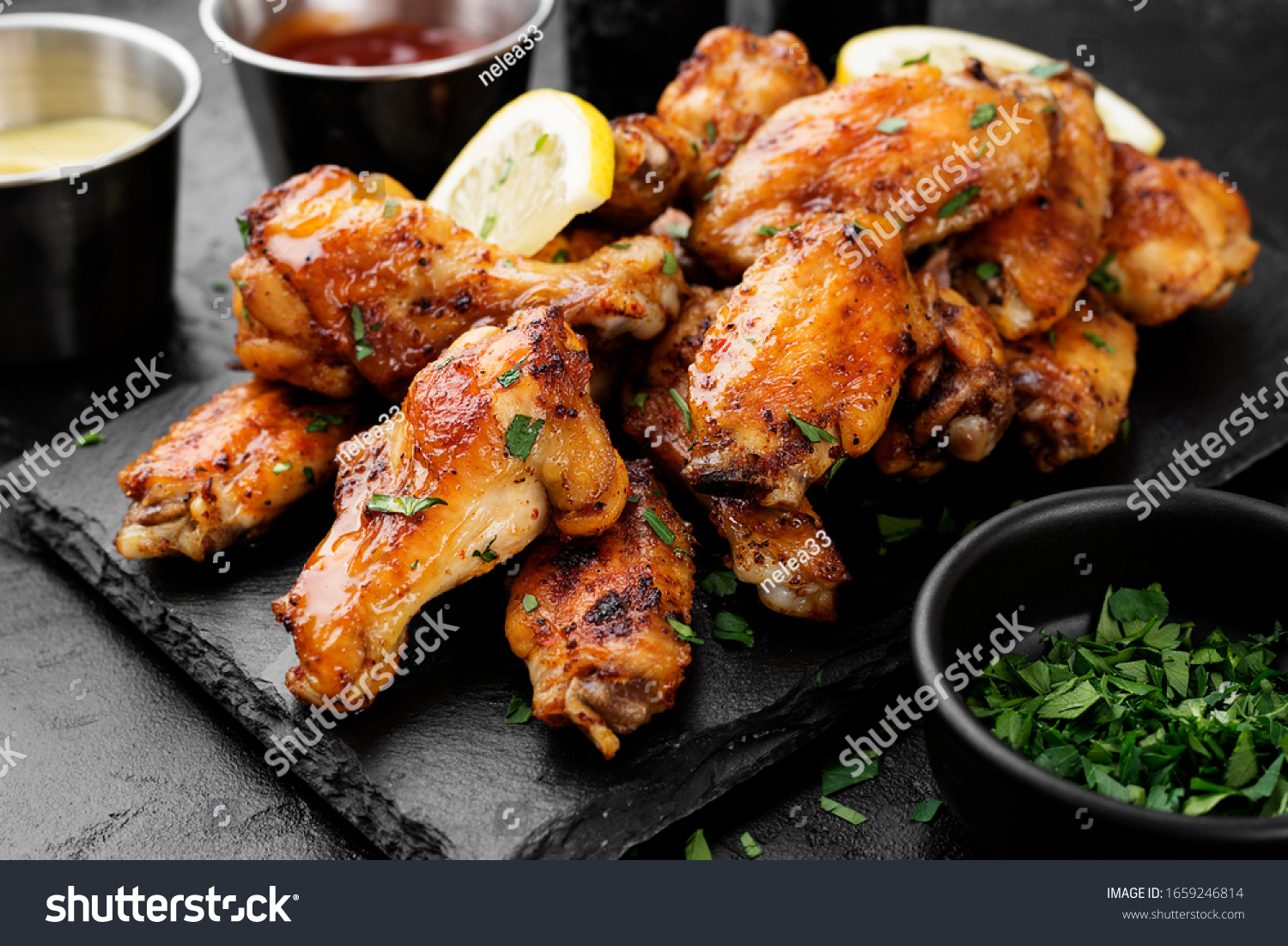 Baked chicken wings served with different sauces and lemon. Black background #1659246814