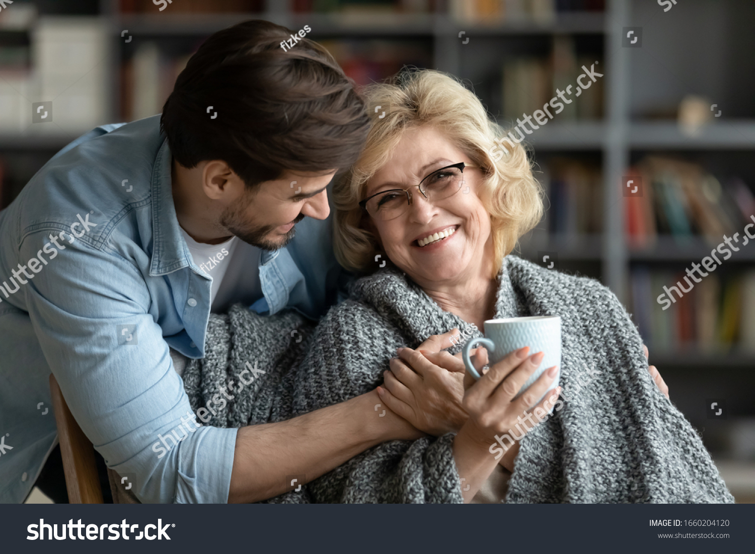 Happy middle-aged mother relax in chair drink tea enjoy family weekend reunion with grown-up son, smiling senior 70s mom rest at home spend time with caring adult man child, bonding concept #1660204120