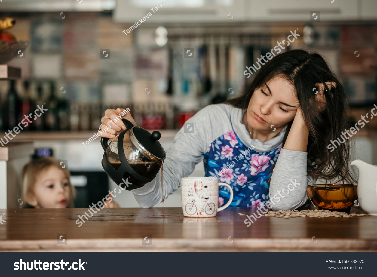 Tired mother, trying to pour coffee in the morning. Woman lying on kitchen table after sleepless night, trying to drink coffee #1660338070
