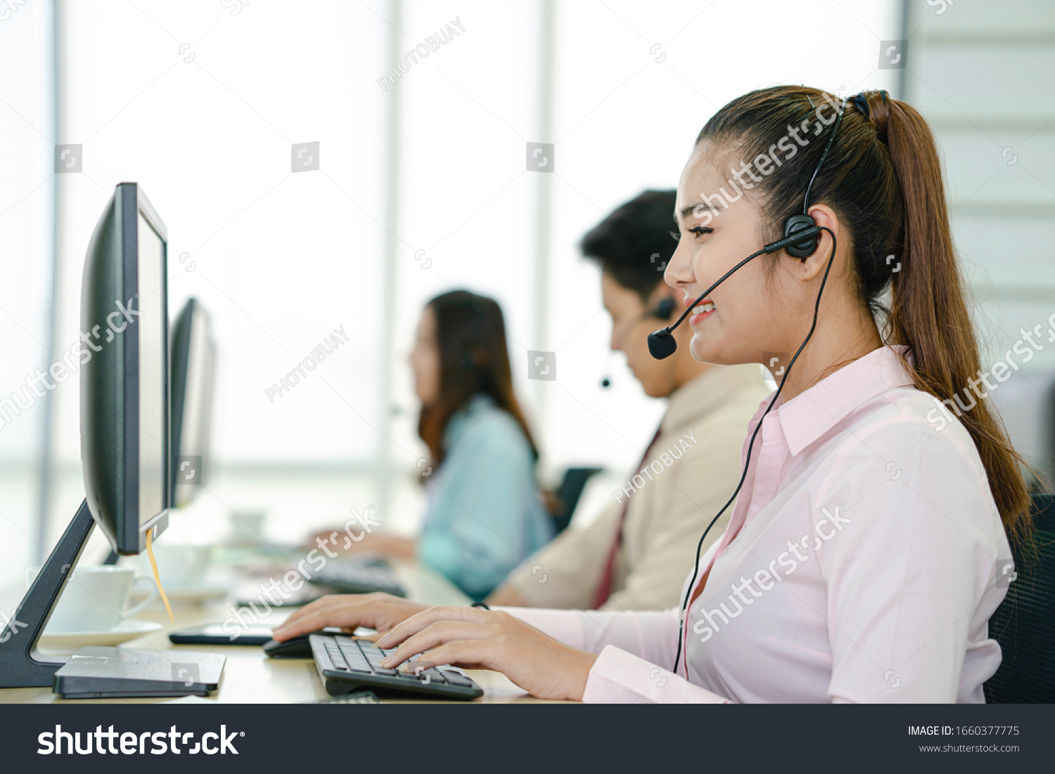 Call center worker accompanied by her team. Smiling customer support operator at work. Young employee working with a headset.
 #1660377775