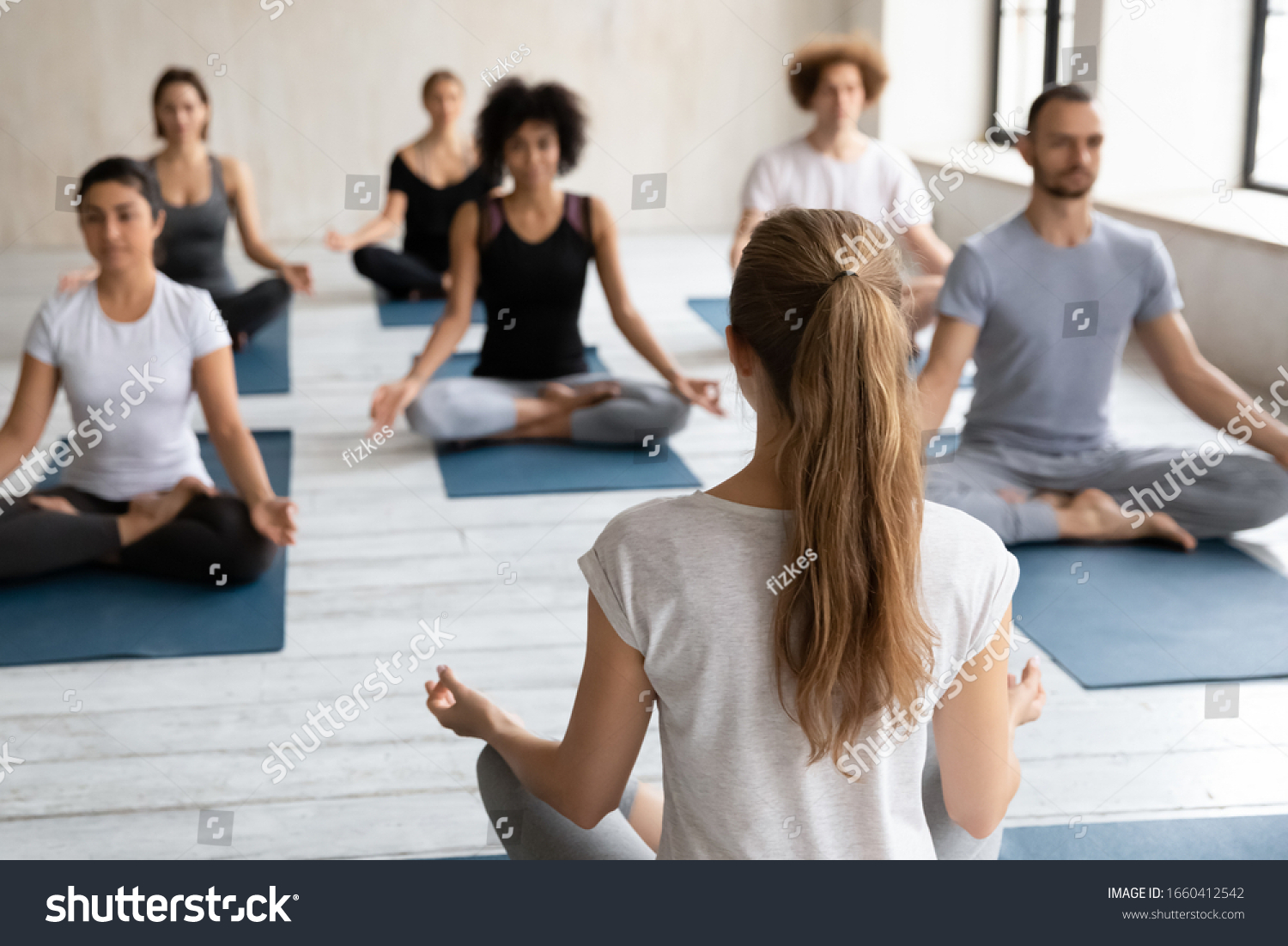 Rear back view woman yoga coach and diverse group of people on background sit in lotus pose do meditation practice, feel sense of calm, peace and inner balance, emotional well-being and health concept #1660412542