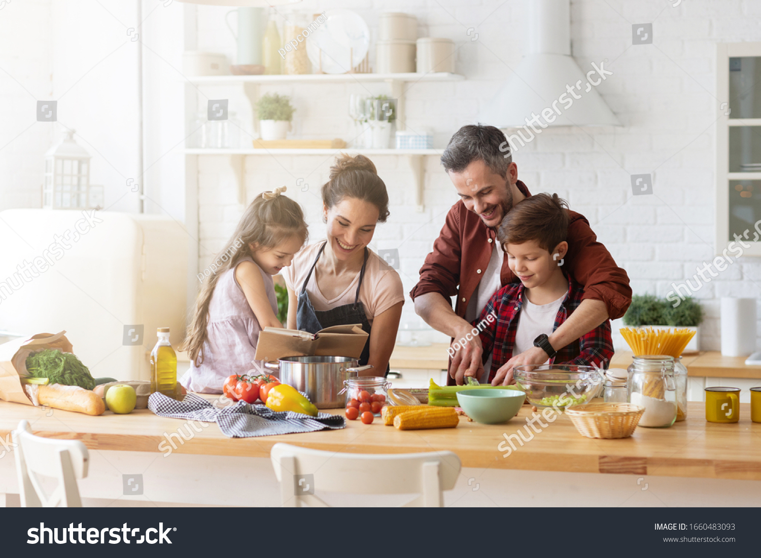 Happy family cooking together on kitchen. Mother and daughter reading recipe to father and son. Dad and boy chopping green vegetable leaf for salad. Home recreation and food preparation on weekend #1660483093
