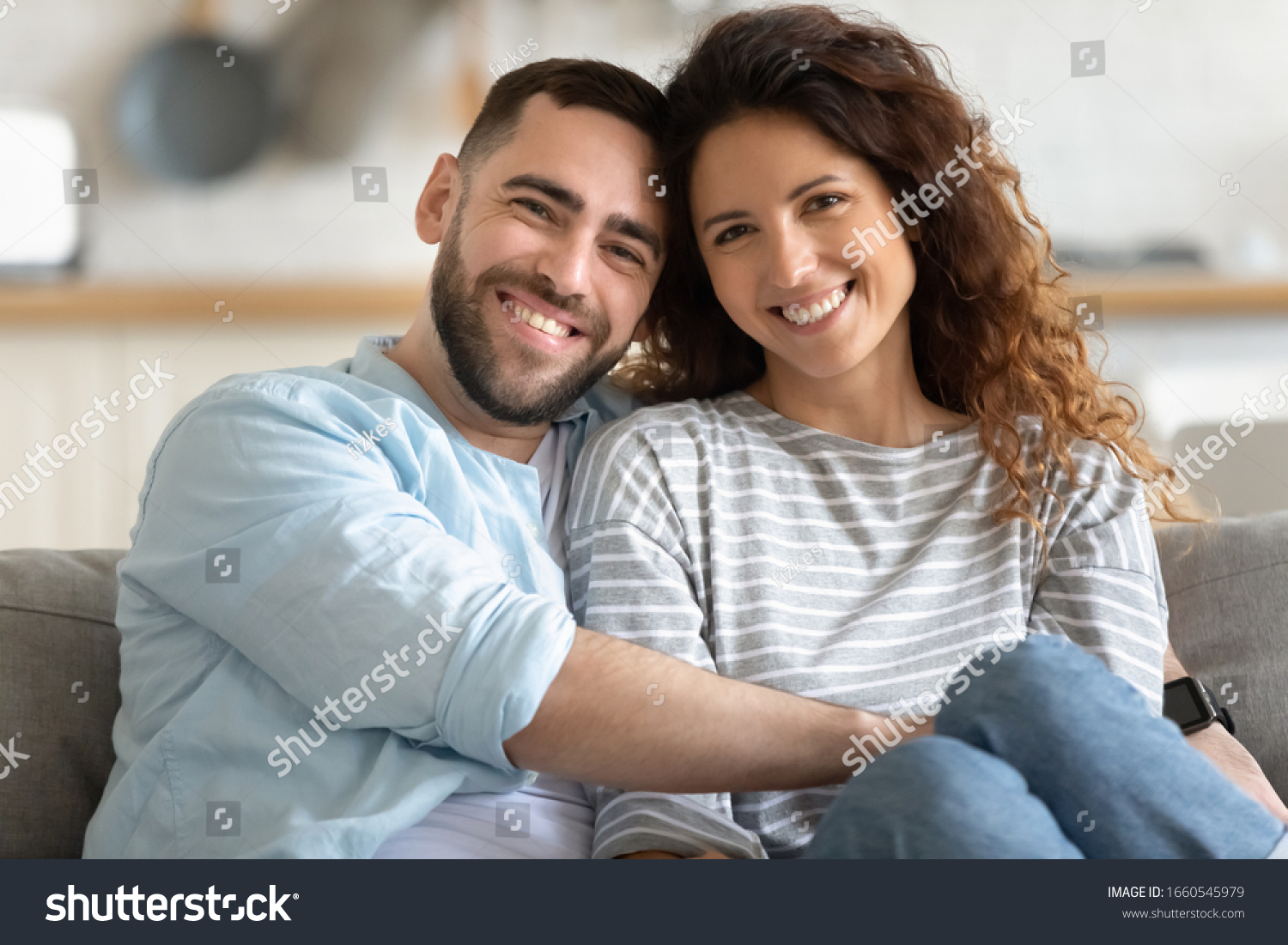 Family portrait of happy millennial husband and wife sit on couch hug cuddle look at camera posing, smiling young couple embrace show love affection, relax at home on weekend together #1660545979