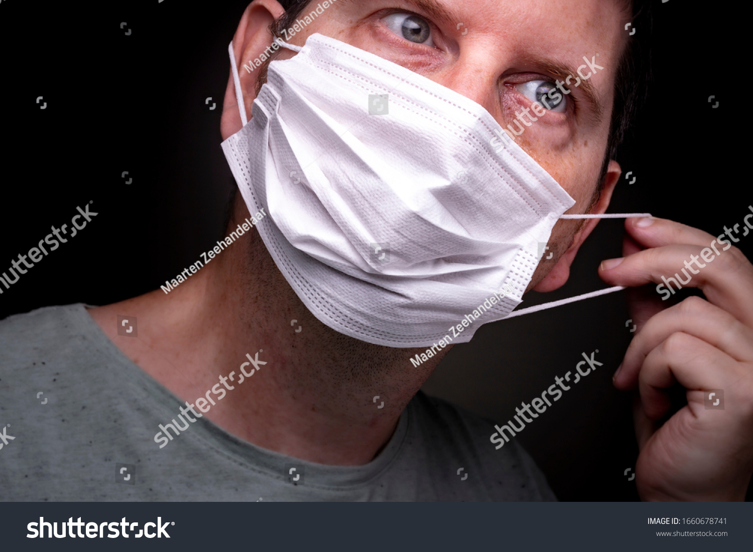 Close up of a caucasian man putting on a medical face mask with one hand stretching the elastic band and putting the protective mouthpiece on #1660678741