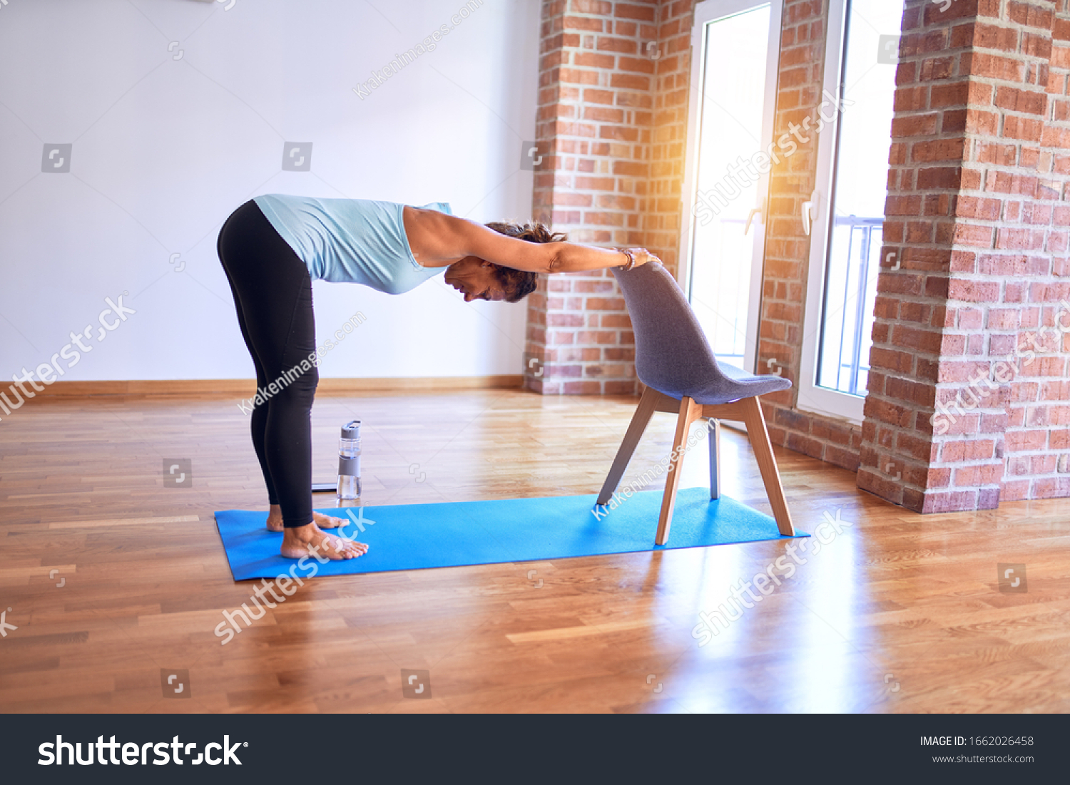 Middle age beautiful sportwoman standing on mat. Practicing yoga doing down dog on chair pose at gym #1662026458