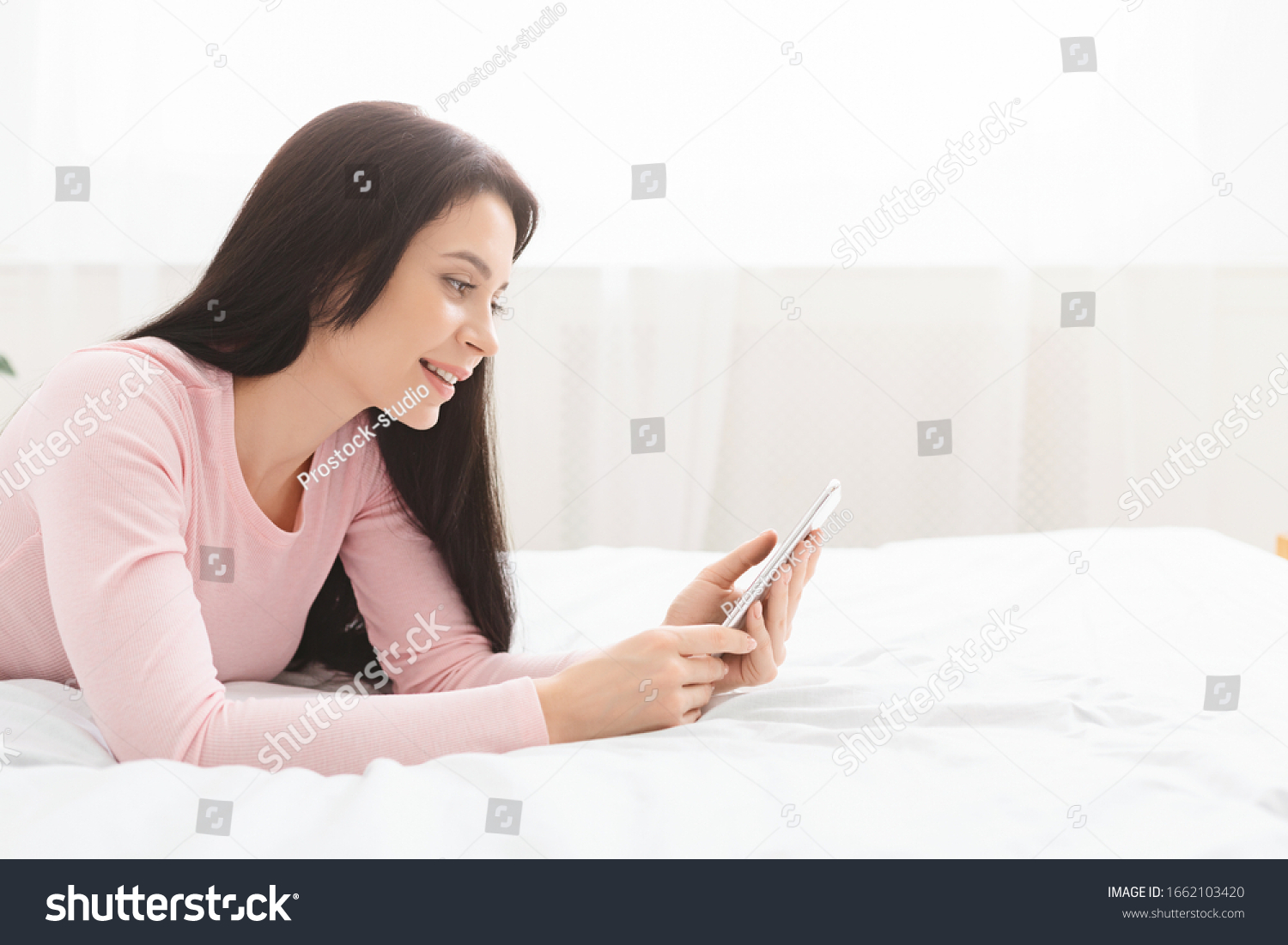 Internet time. Millennial woman browsing on cellphone, lying on bed, side view, empty space #1662103420