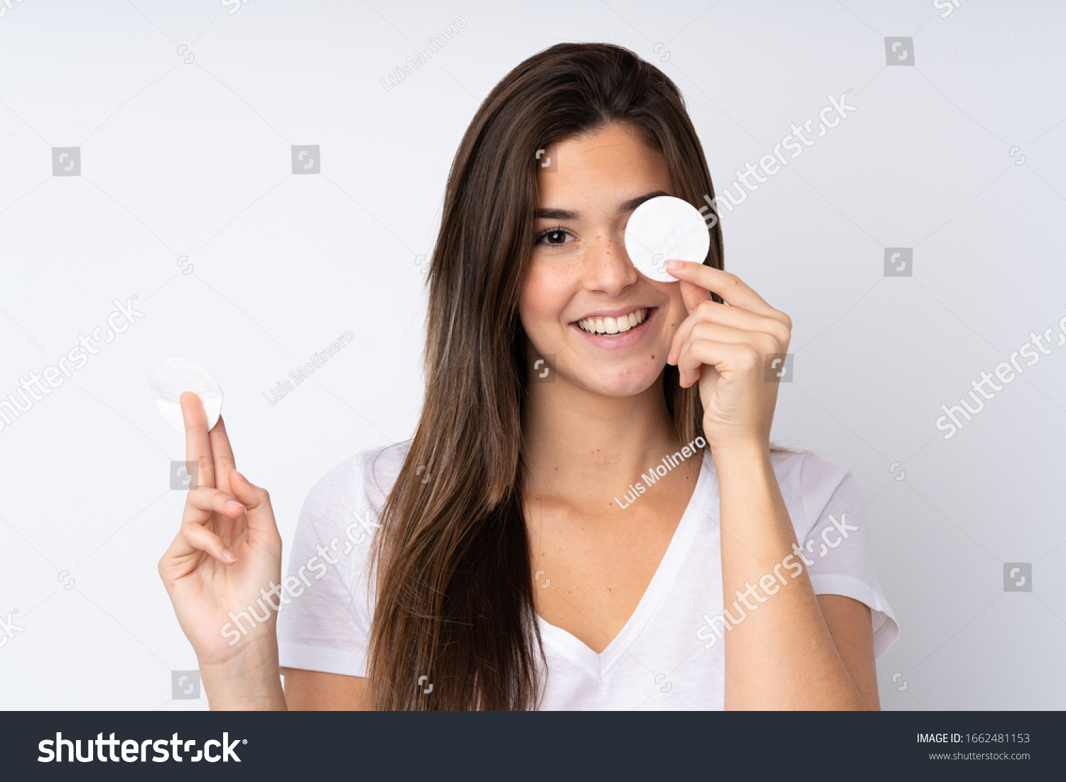 Teenager girl over isolated background with cotton pad for removing makeup from her face and smiling #1662481153