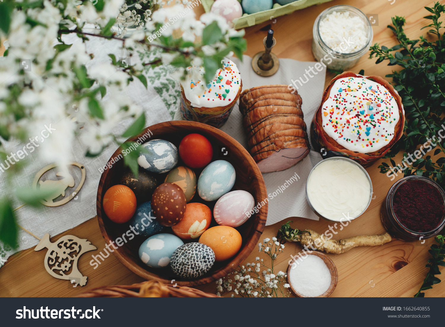 Easter food flat lay. Easter eggs natural dyed, easter bread, ham, beets, butter, green branches and flowers on rustic wooden table. Traditional Easter Food for breakfast #1662640855