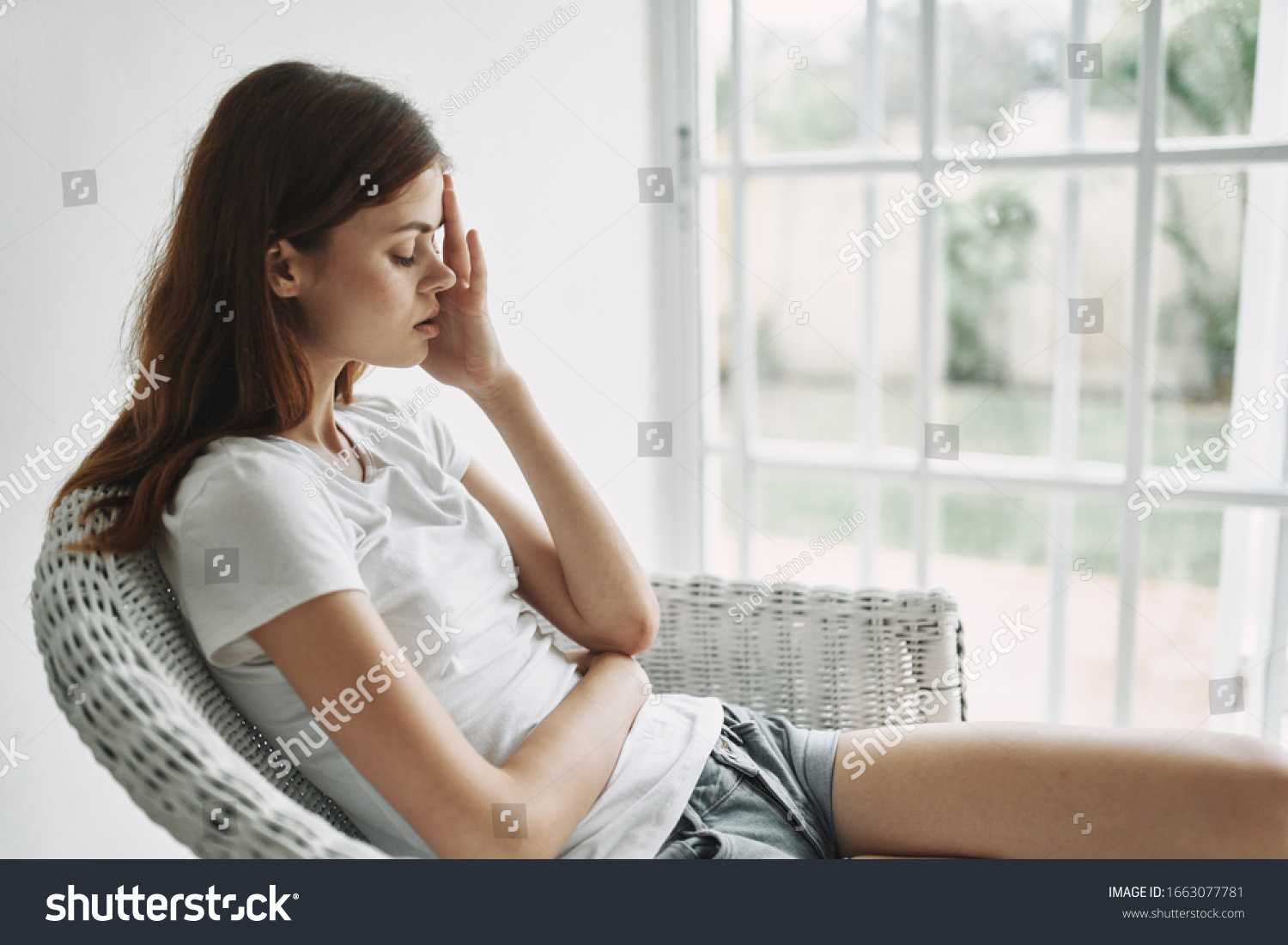 A woman sits in a chair touches her head with her hand #1663077781