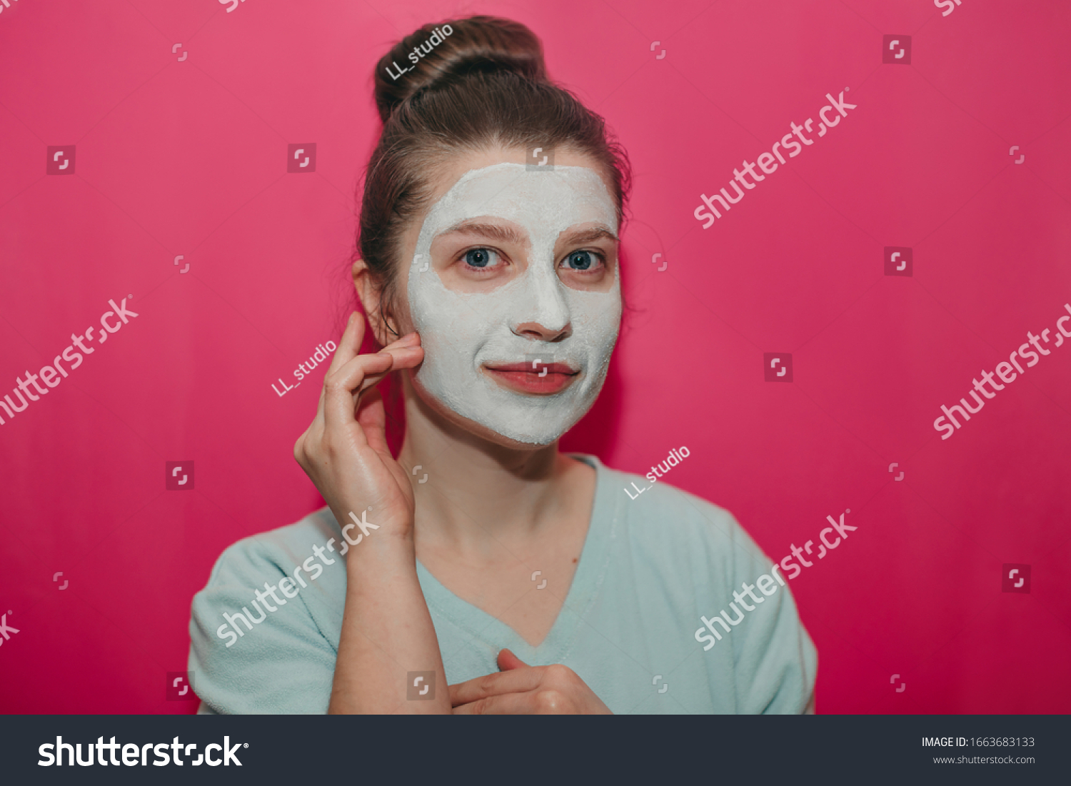 Young beautiful girl with big blue eyes smiling hands near face, with a white clay mask on her face and hair bumps on a pink background  #1663683133