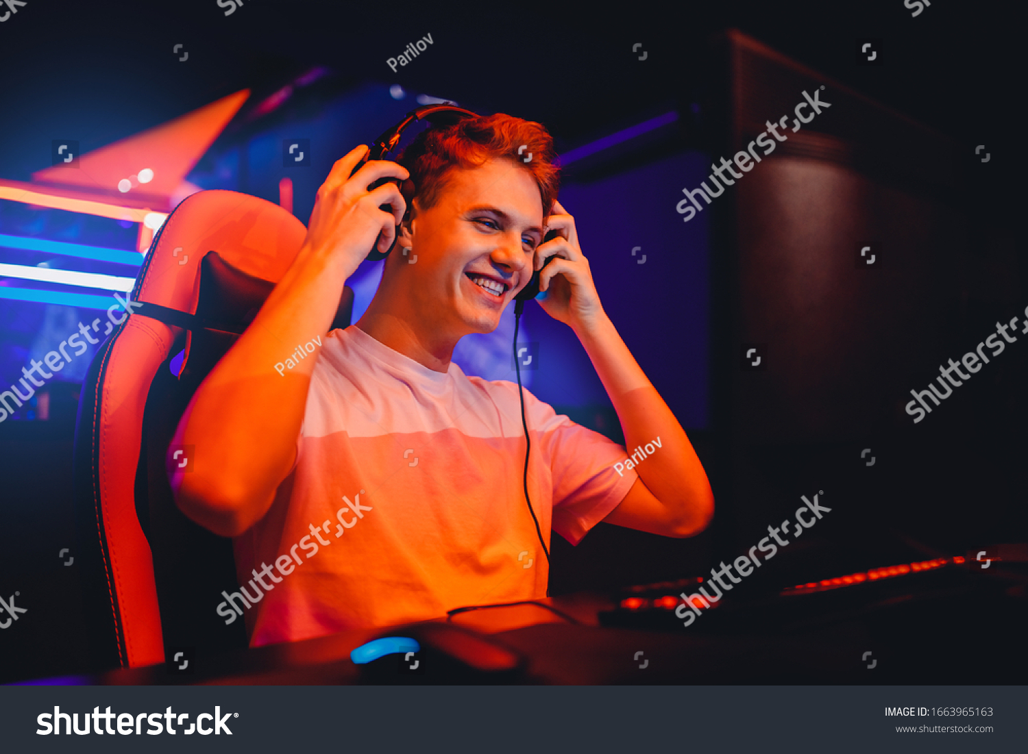 Streamer young man rejoices in victory professional gamer playing online games computer with headphones, neon color. #1663965163