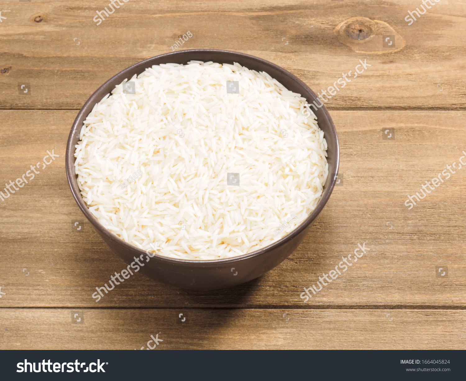 Long grain Basmati rice in brown ceramic bowl on brown wooden background #1664045824