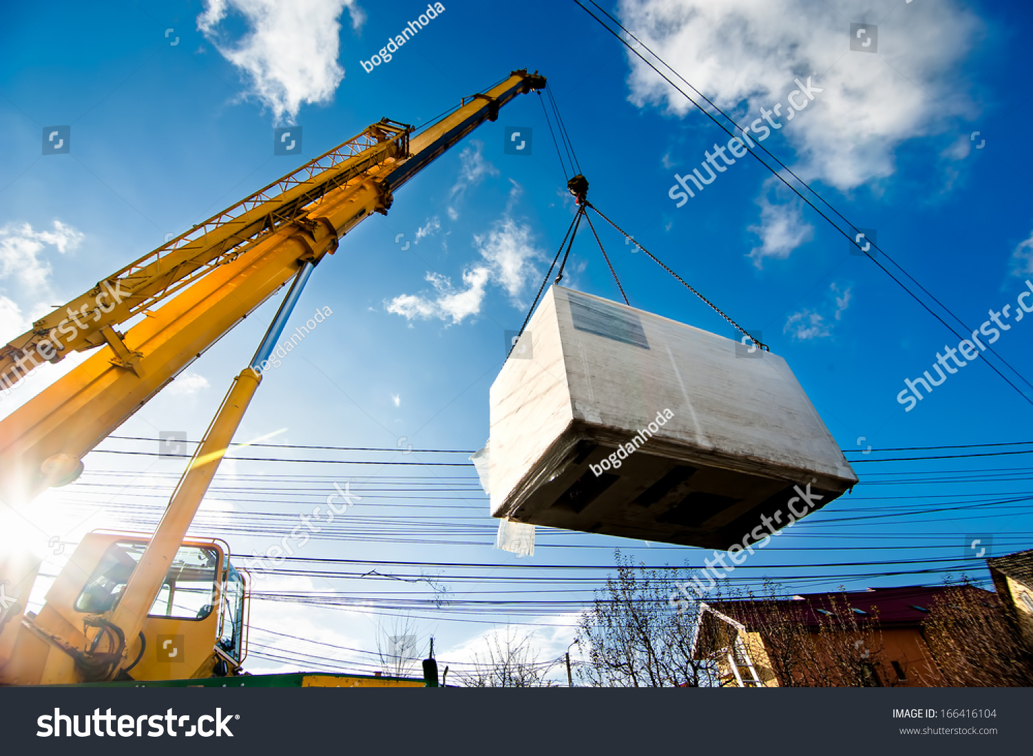 Industrial Crane operating and lifting an electric generator against sunlight and blue sky #166416104