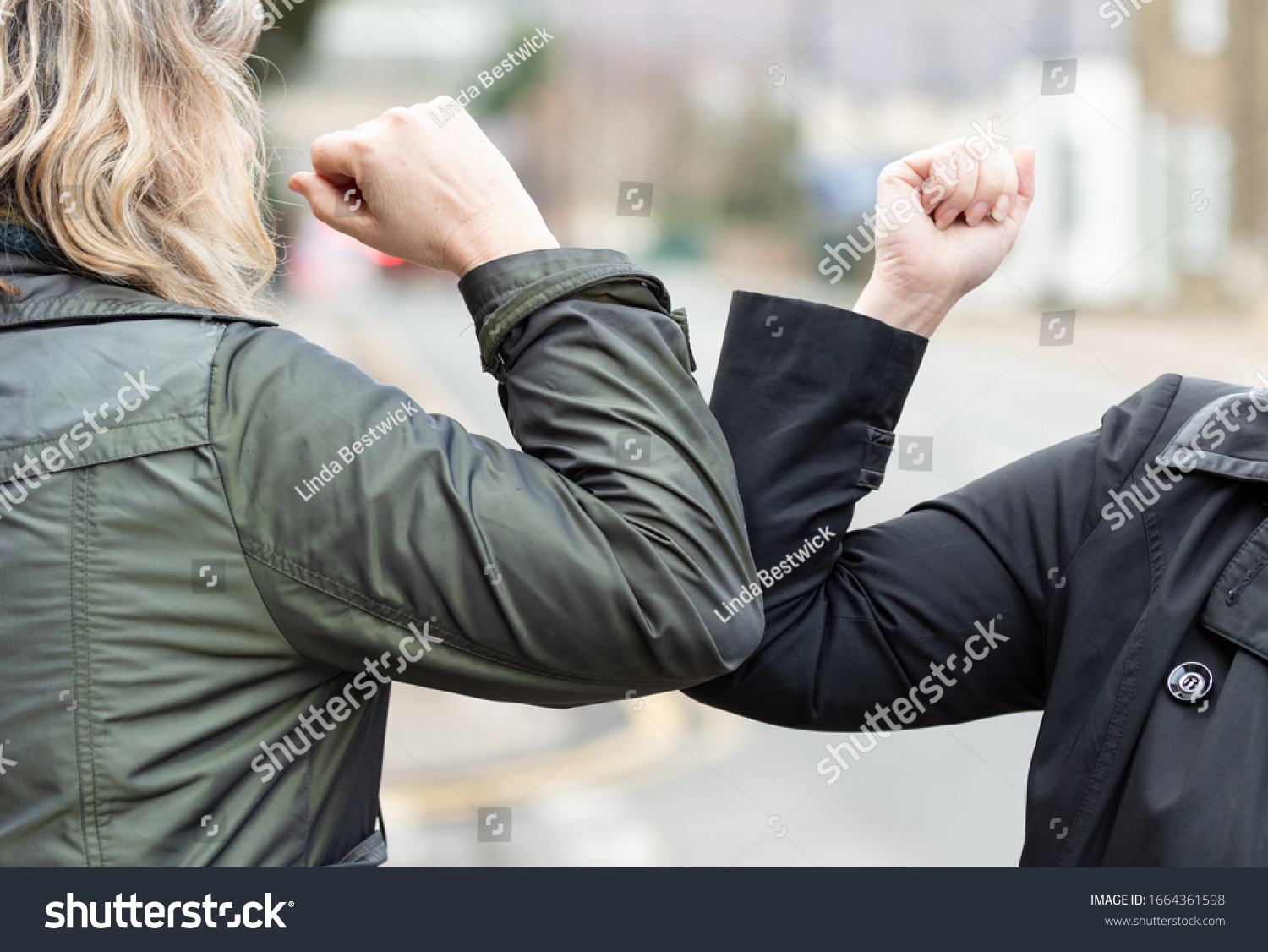 Elbow bump. New novel greeting to avoid the spread of coronavirus. Two women friends meet in a British street with bare hands. Instead of greeting with a hug or handshake, they bump elbows instead. #1664361598