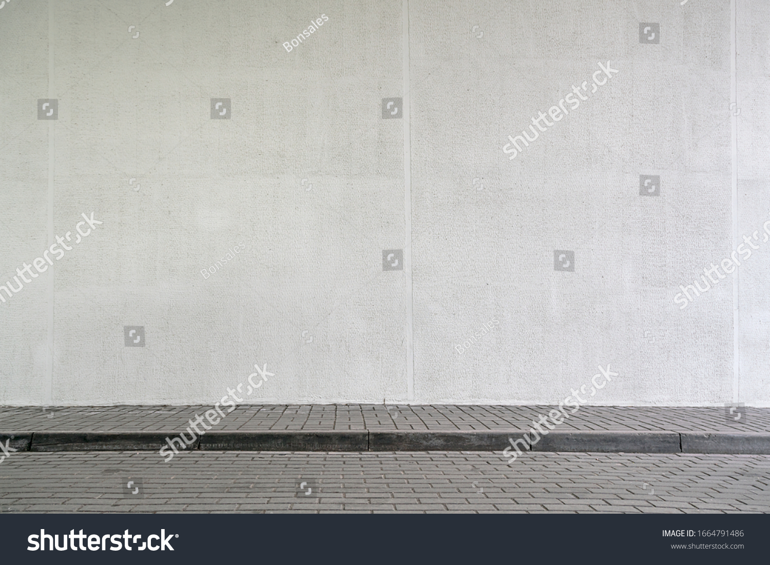 large modern building with high white wall near empty sidewalk covered with grey stone tiles on city street in spring #1664791486