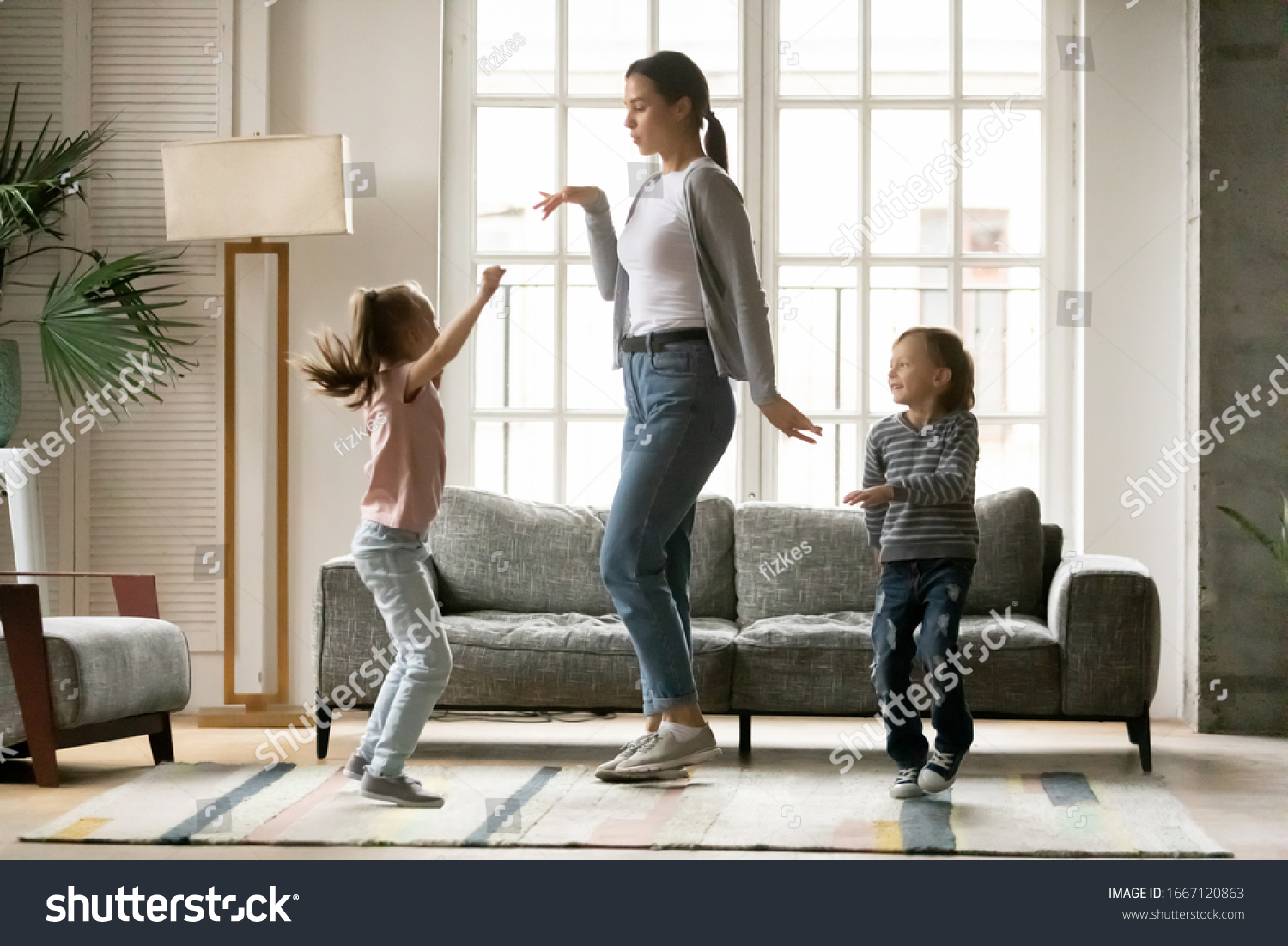 Full length happy young mother dancing with small children siblings in living room. Small energetic kids brother sister having fun with positive nanny together at home, enjoying daycare time. #1667120863