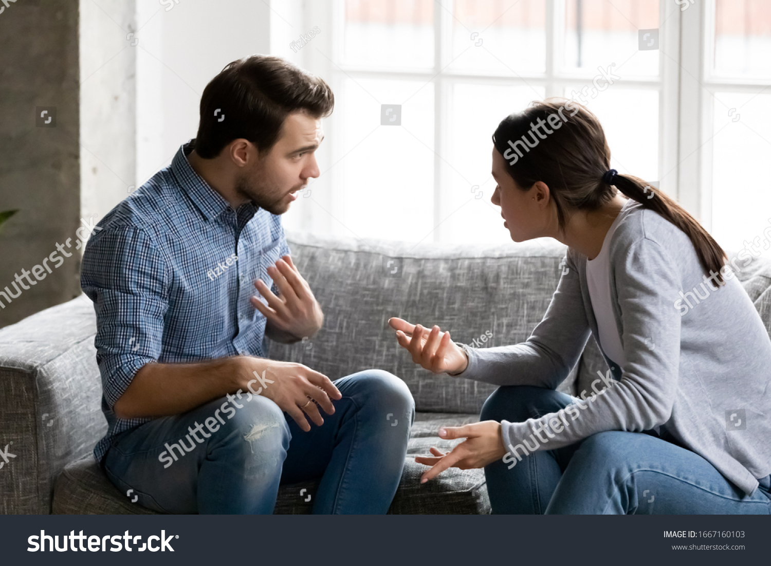 Stressed young married family couple arguing emotionally, blaming lecturing each other, sitting on couch. Depressed husband quarreling with wife, having serious relations communication problems. #1667160103