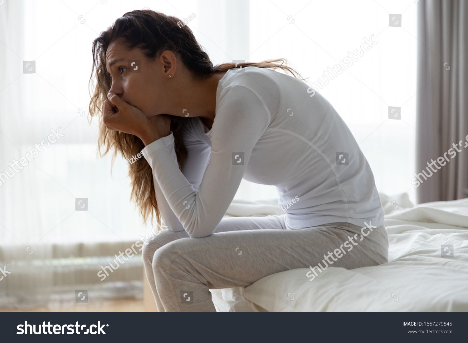 Upset millennial girl sit on bed in bedroom lost in thoughts thinking pondering of problem solution, depressed unhappy young woman look in distance suffer from depression, having personal problems #1667279545