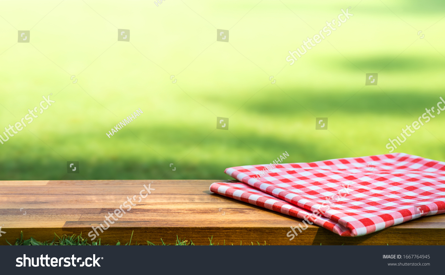 Red checked tablecloth on wood with blur green courtyard background.Summer and picnic concepts.Design for key visual food and drink products.no people #1667764945