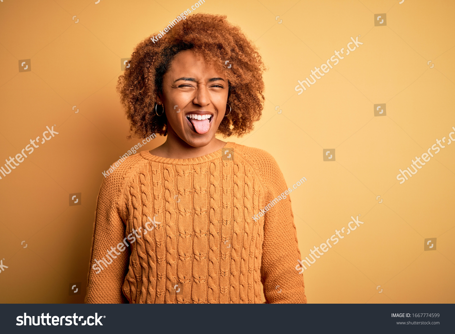 Young beautiful African American afro woman with curly hair wearing casual sweater sticking tongue out happy with funny expression. Emotion concept. #1667774599