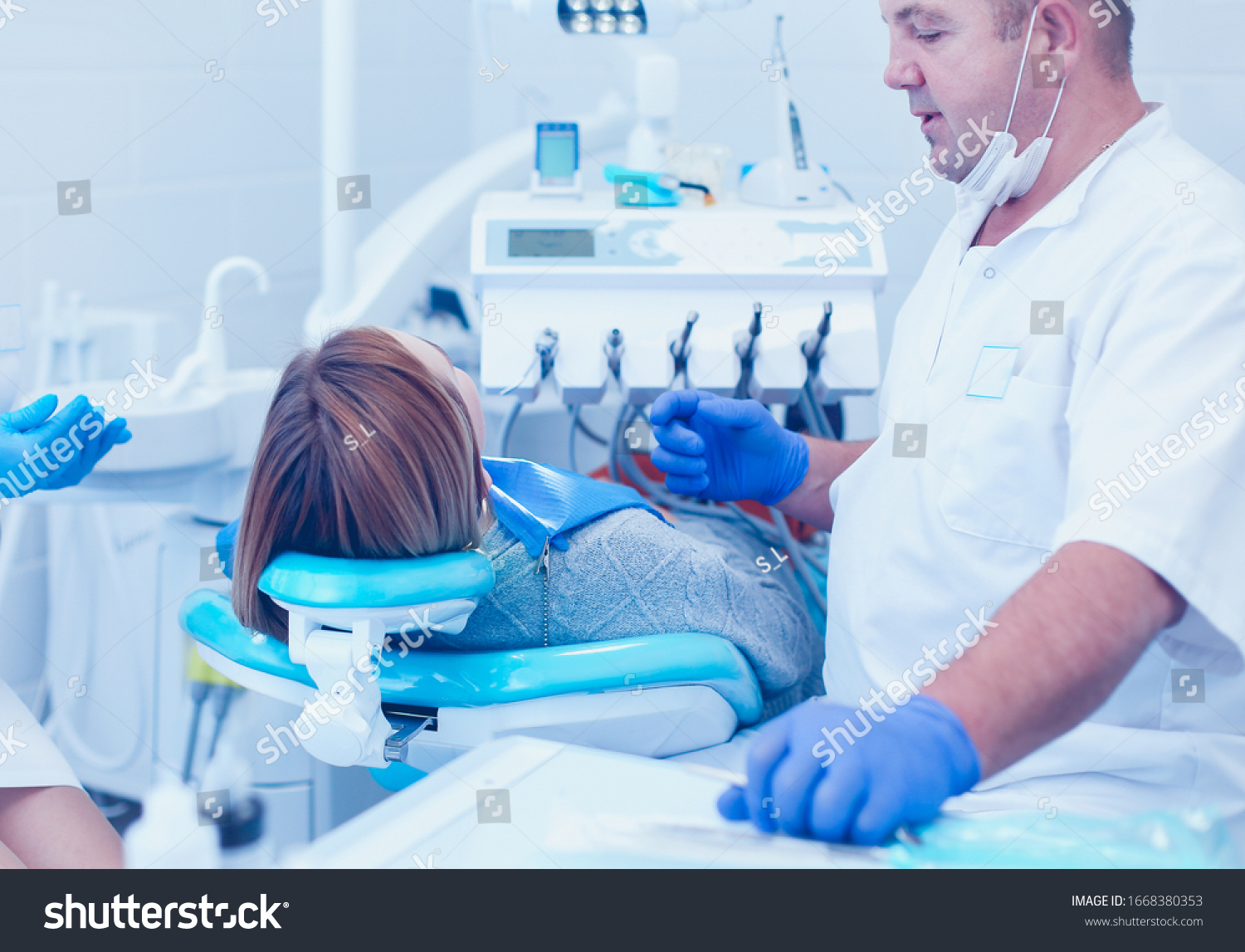 Senior male dentist in dental office talking with female patient and preparing for treatment #1668380353