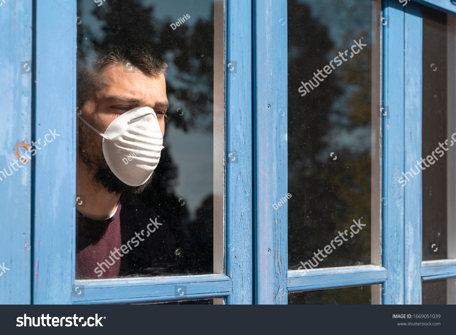Coronavirus. Sick man of corona virus 
looking through the window and wearing mask protection and recovery from the illness in home. Quarantine. Patient isolated to prevent infection. Lockdown #1669051039