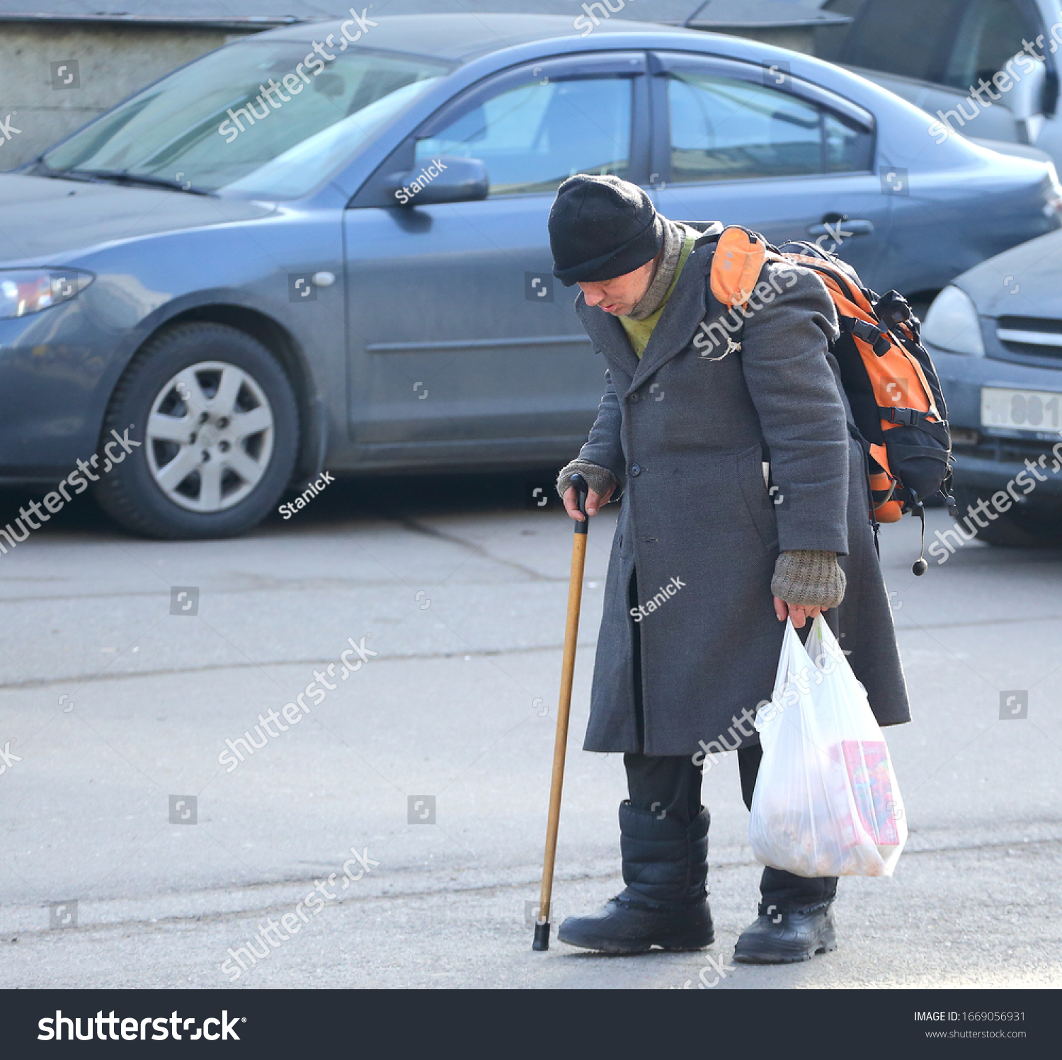 A homeless tramp with a stick walks through the Parking lot, Bolshevikov Avenue, Saint Petersburg, Russia, March 2020 #1669056931