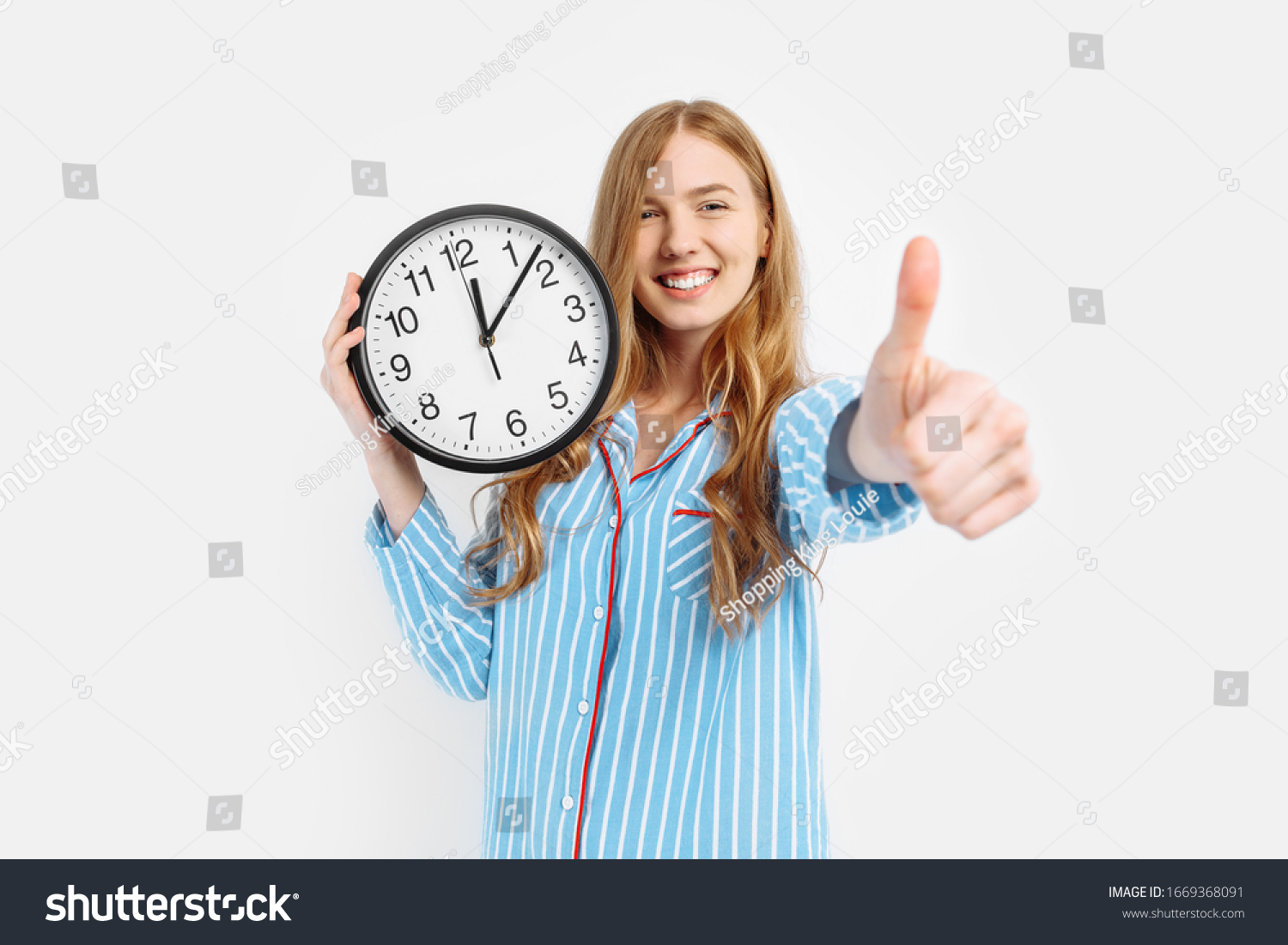Happy girl wearing pajamas holding an alarm clock shows the gesture a class, waking early in the morning on a white background #1669368091