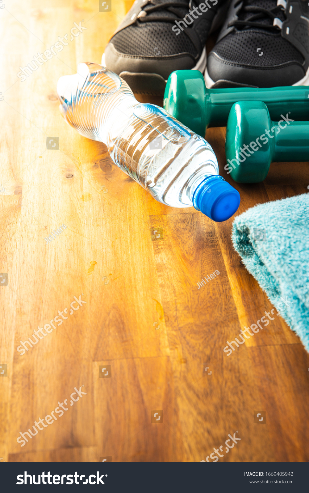 Fitness concept. Black sports shoes, dumbbell and bottle of water on wooden floor. #1669405942