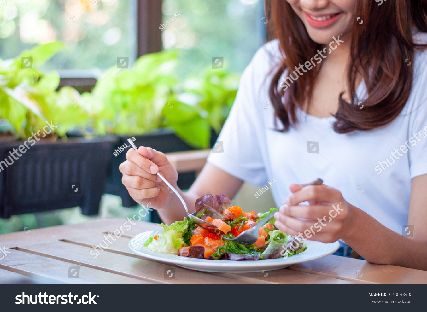 The smiling woman enjoys eating a salmon salad. To lose weight and diet, eat foods that are beneficial to the body. Weight loss concept. #1670098900
