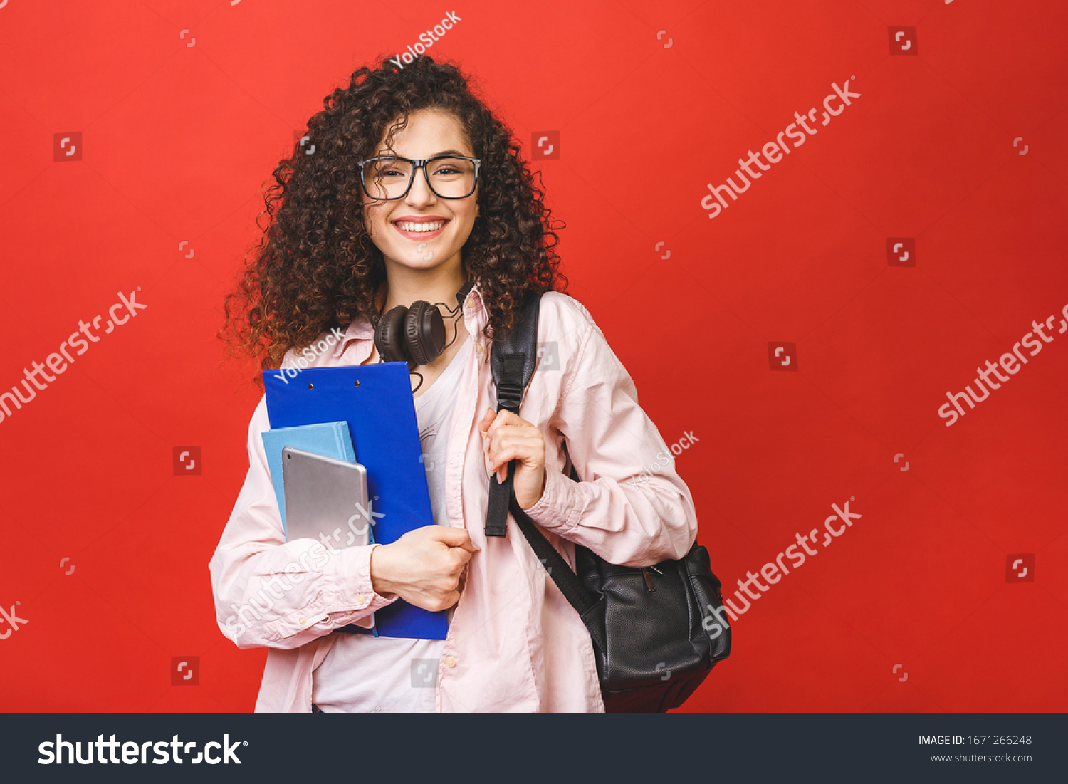 Young curly student woman wearing backpack glasses holding books and tablet over isolated red background.  #1671266248