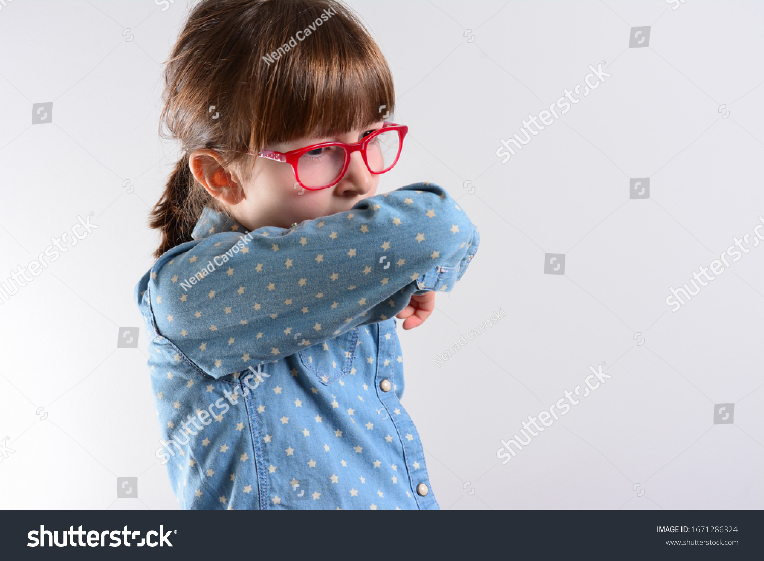 Unhappy kid Cough into her elbow, not her hand. Small girl pull the collar of her T-shirt up to cover mouth when coughing. Coughing advice from experts who seek to minimize risk of viral transmission #1671286324