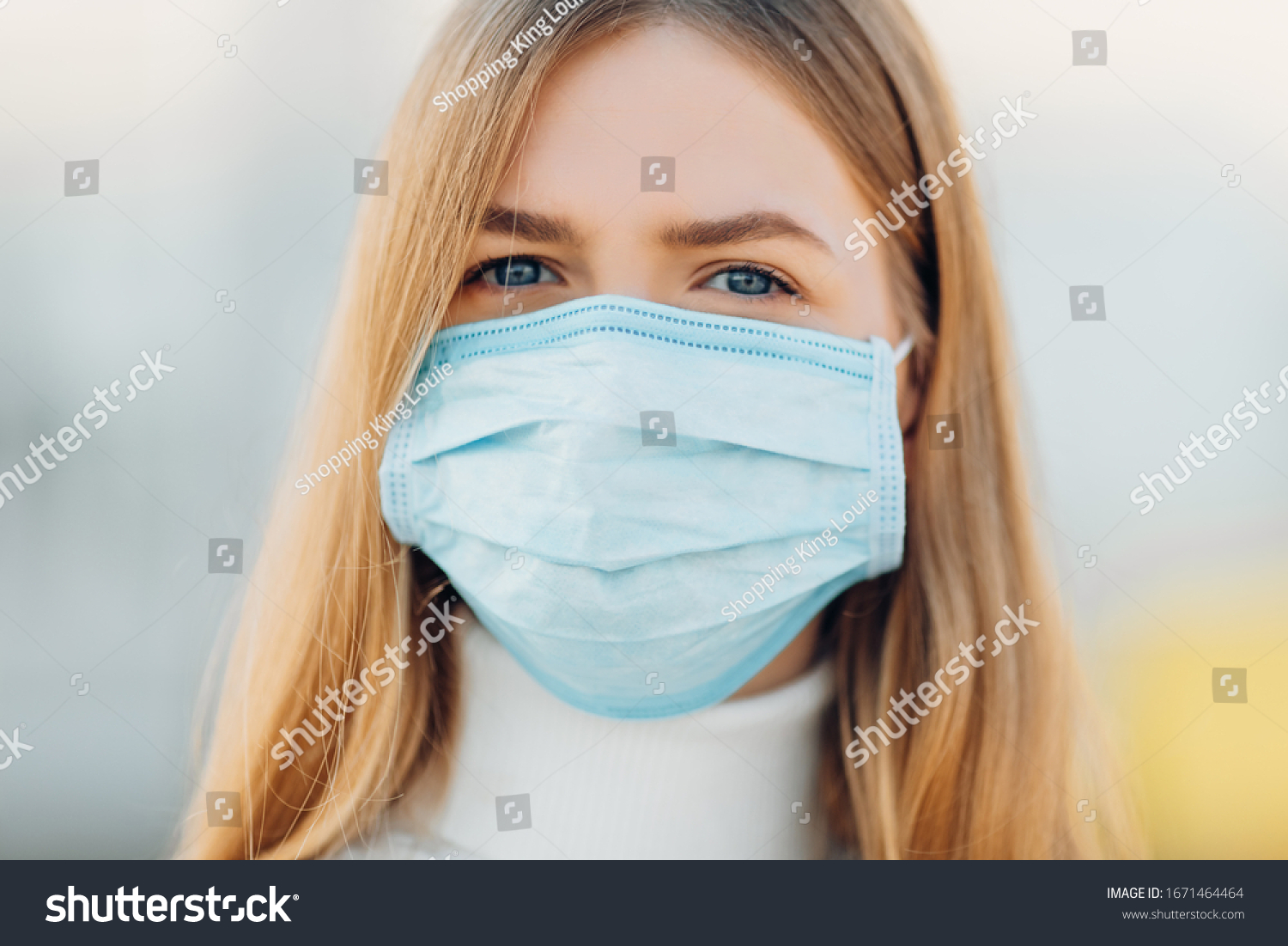 A young girl in the background of a building wears a face mask that protects against the spread of coronavirus disease. Close- up of a young woman with a surgical mask on her face against SARS-cov-2. #1671464464