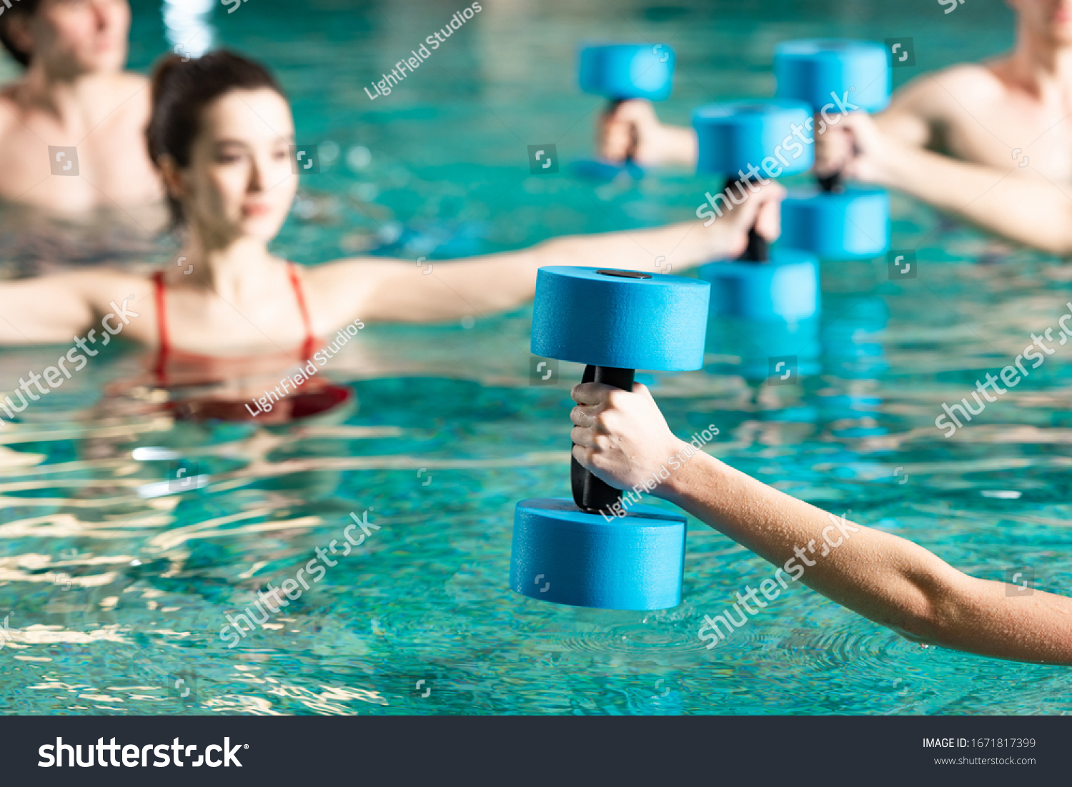 Selective focus of trainer with barbell working out with people in swimming pool #1671817399