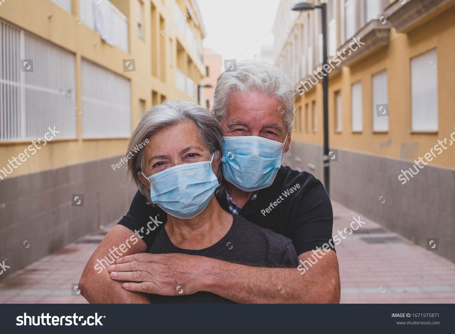 couple of two seniors wearing medical mask to prevent coronavirus (covid-19) or another type of virus - close up of faces in middle of street -  protect happy cheerful people looking at the camera fun #1671975871