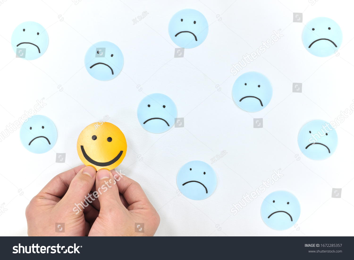 A smiling face icon among a group of sad emoticons in white background. Be positive and stay happy concept. #1672285357
