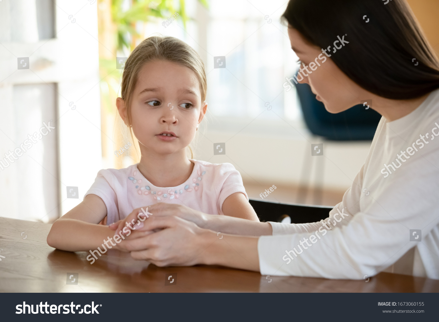 Head shot unhappy small child girl sitting at table with worrying mother, sharing school problems. Compassionate caring attentive mommy having trustful conversation with unhappy offended daughter. #1673060155