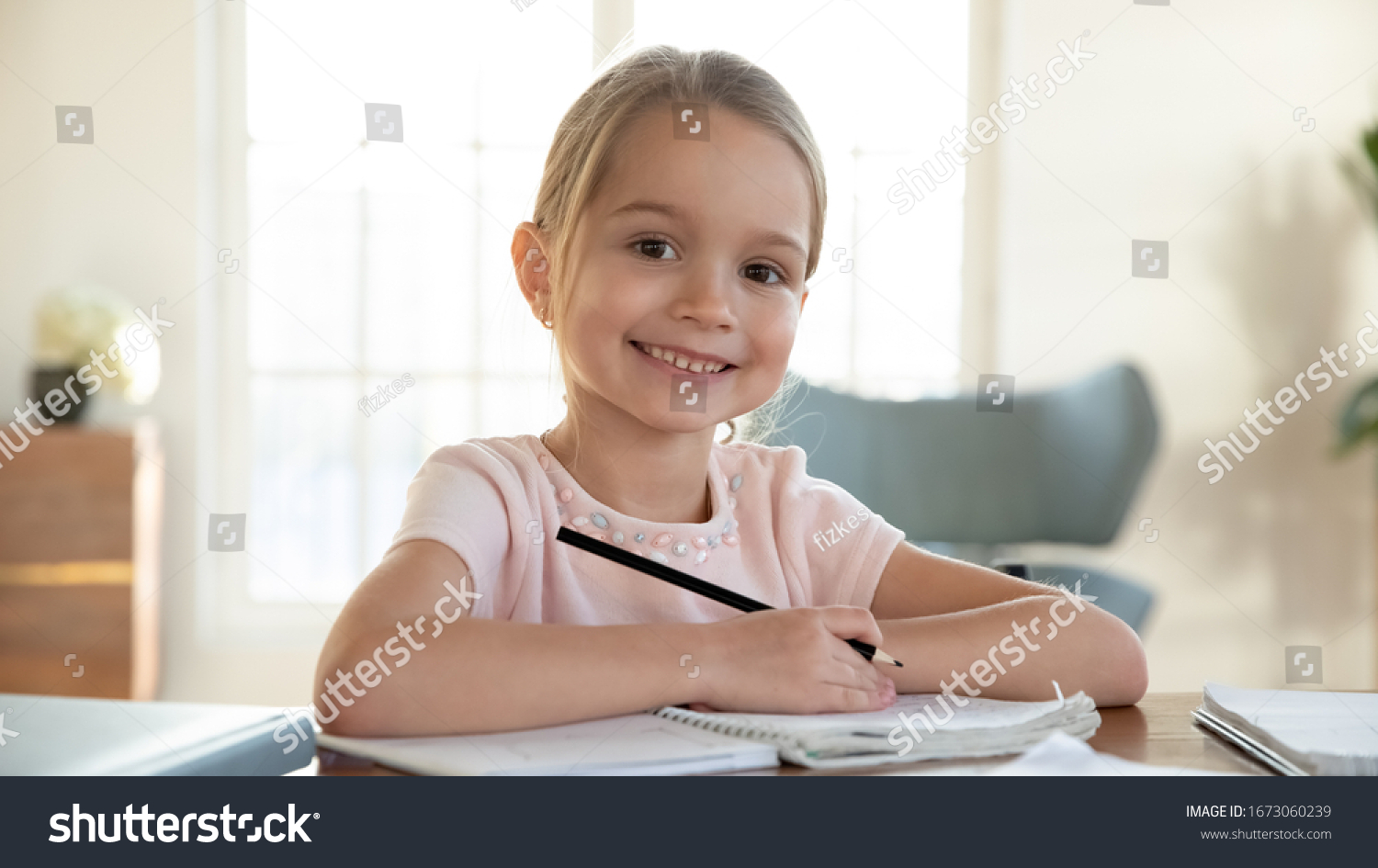 Head shot close up portrait of happy small pupil learning at home. Smiling little child girl enjoying doing lessons in living room. Smart kid schoolgirl looking at camera, studying remotely online. #1673060239