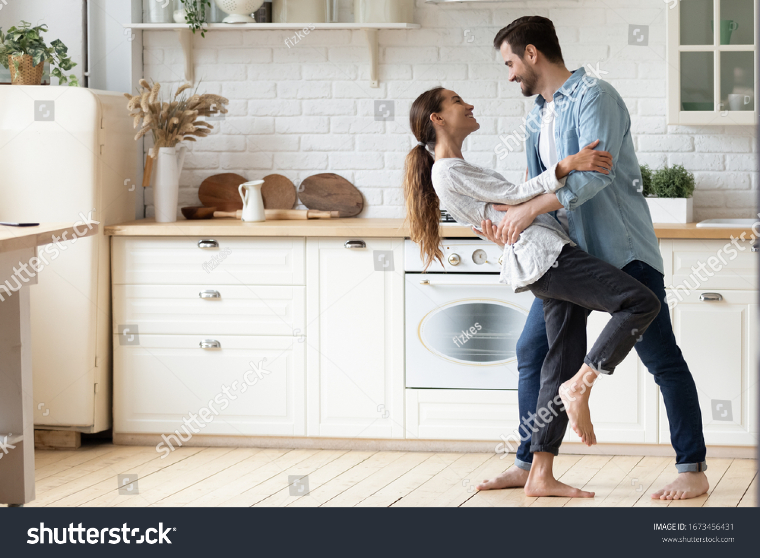 Happy loving young couple dancing romantic dance on date in modern kitchen, smiling husband and wife celebrating anniversary, enjoying tender moment, having fun, moving to music at home #1673456431