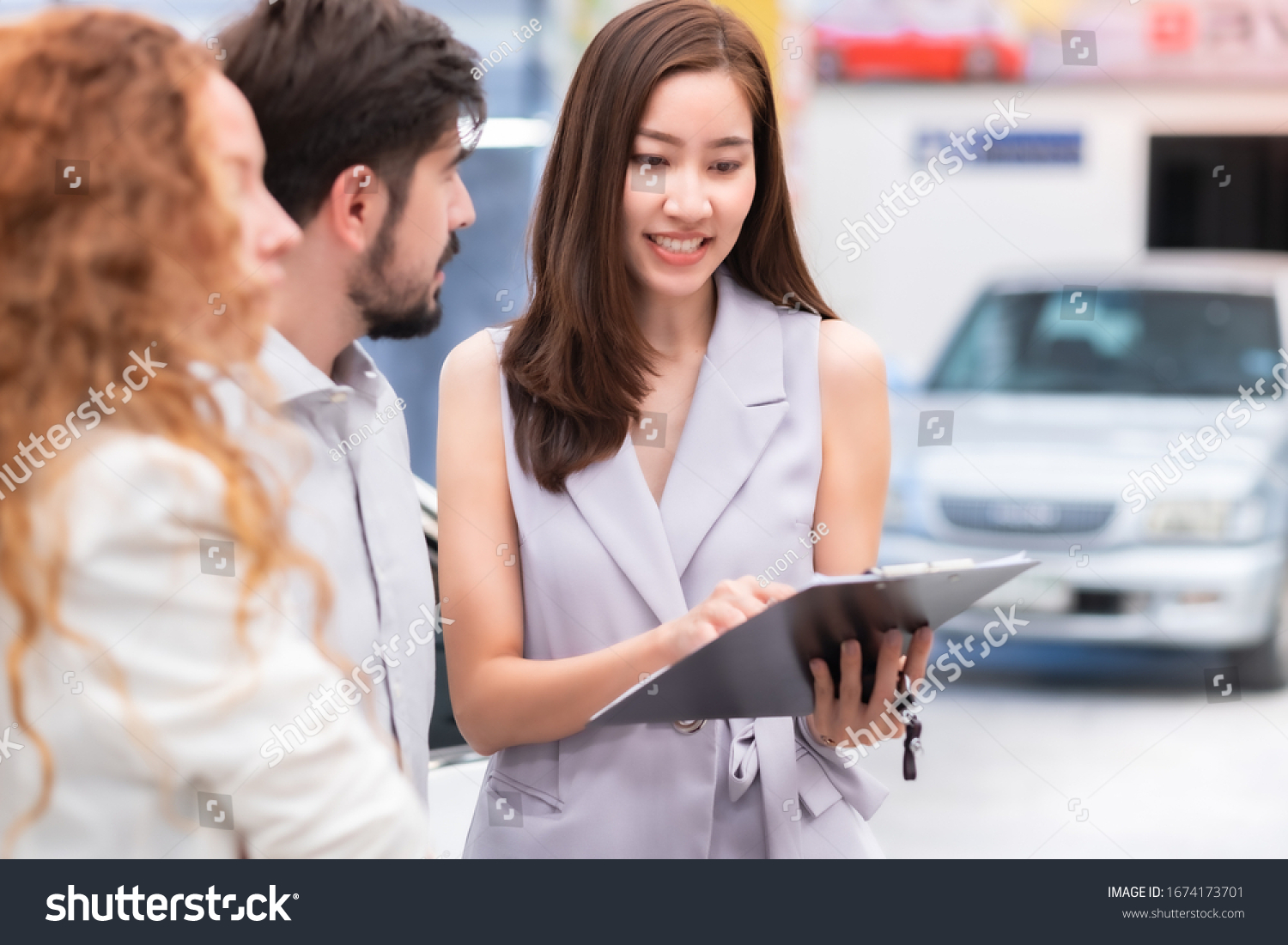 Salesperson working at car dealership.Young Asian woman consultant and couple buyers signing contract for new car in auto show. Concept for car rental or sale. #1674173701