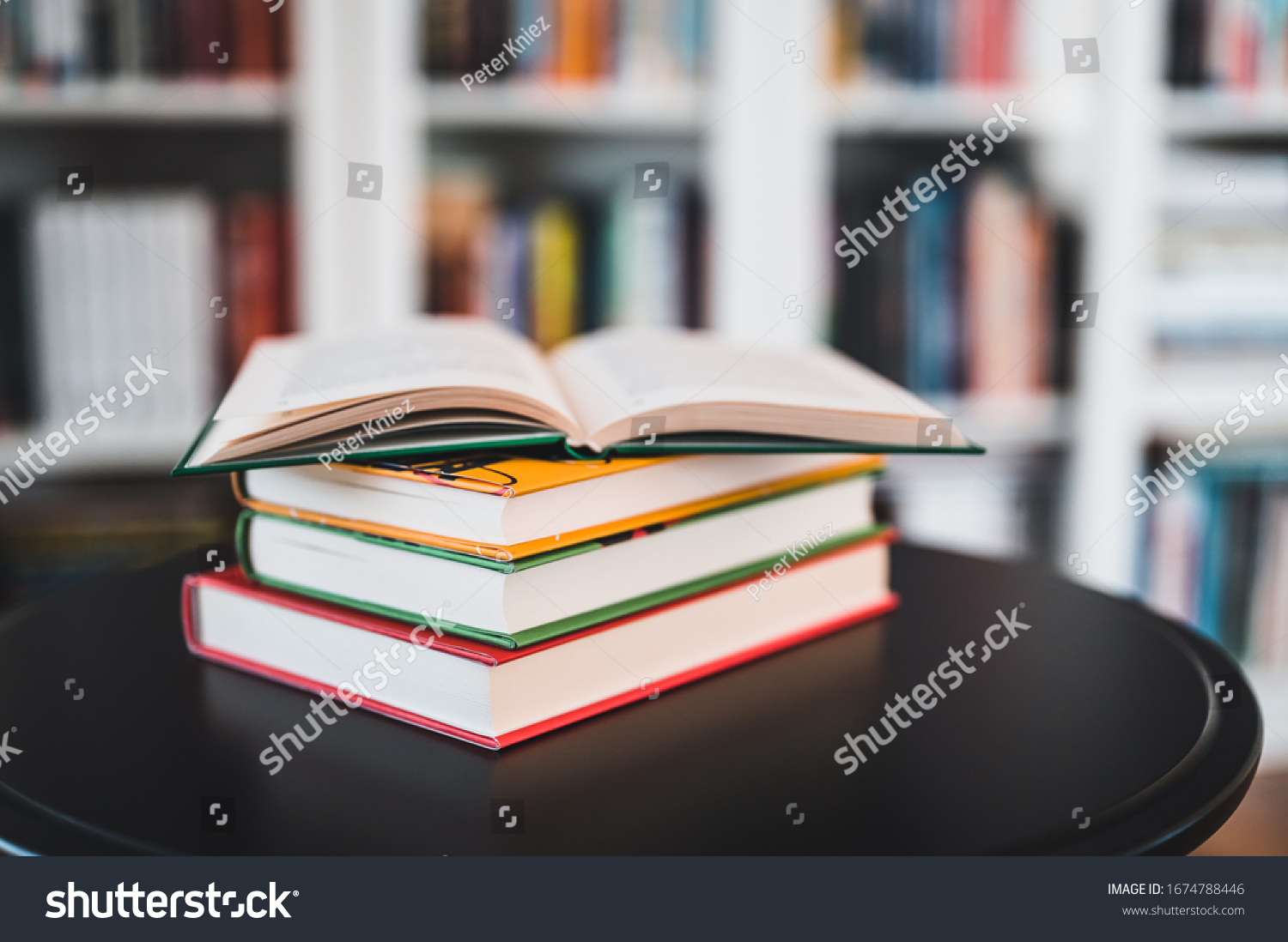 A stack of books on a black table. Library in the background. Stack of books close up. #1674788446
