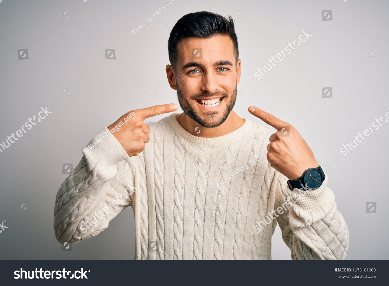 Young handsome man wearing casual sweater standing over isolated white background smiling cheerful showing and pointing with fingers teeth and mouth. Dental health concept. #1675181203