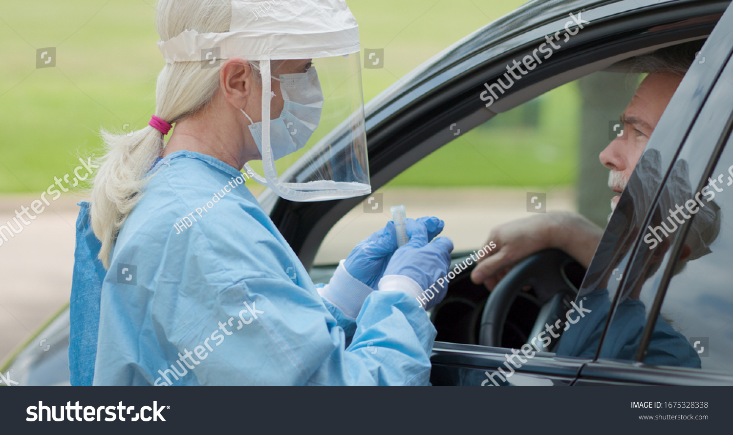 Dressed in full protective gear a healthcare worker collects a sample from a mature man sitting inside his car as part of the operations of a coronavirus mobile testing unit. #1675328338